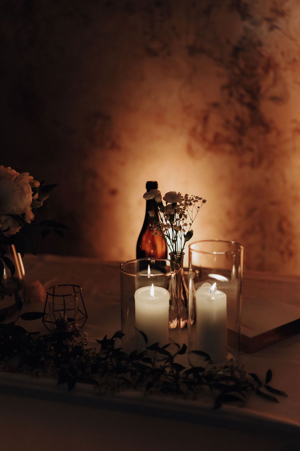 Elegant wedding table decor with white pillar candles, dried flowers, and a vintage bottle.
