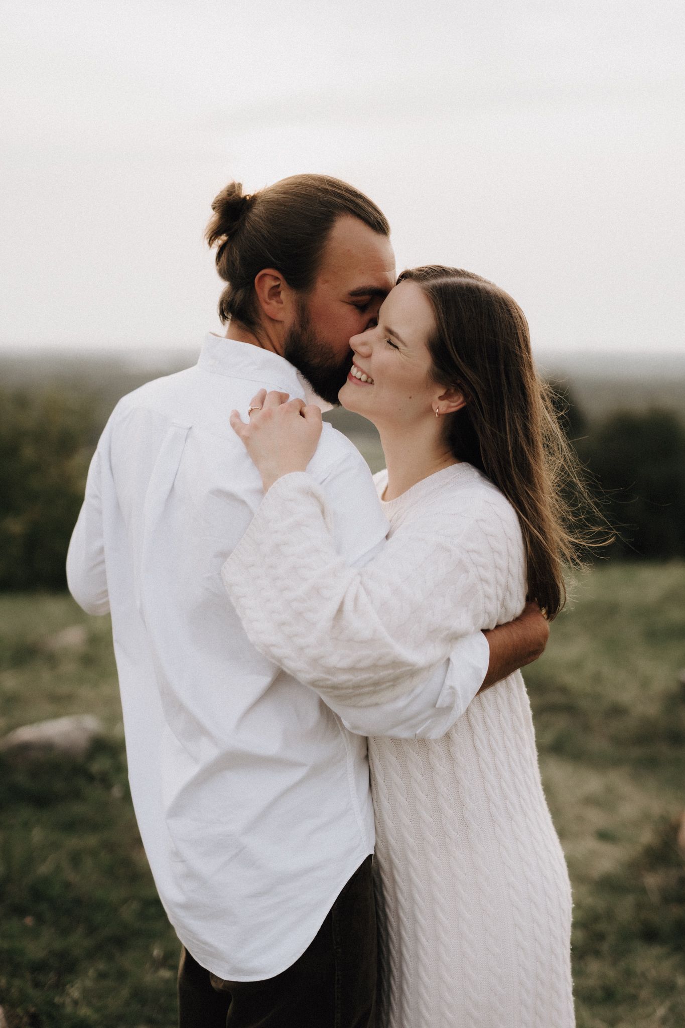 Couple in white outfits embracing and smiling at each other in a green outdoor field.