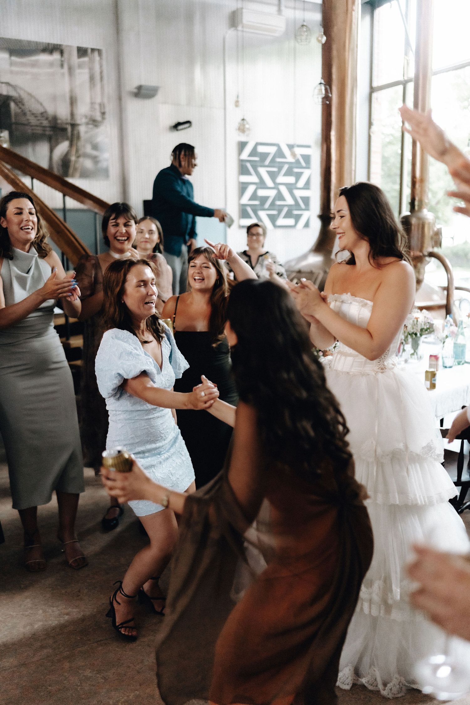 Bride in white ruffled gown dancing and celebrating with female guests at wedding reception.
