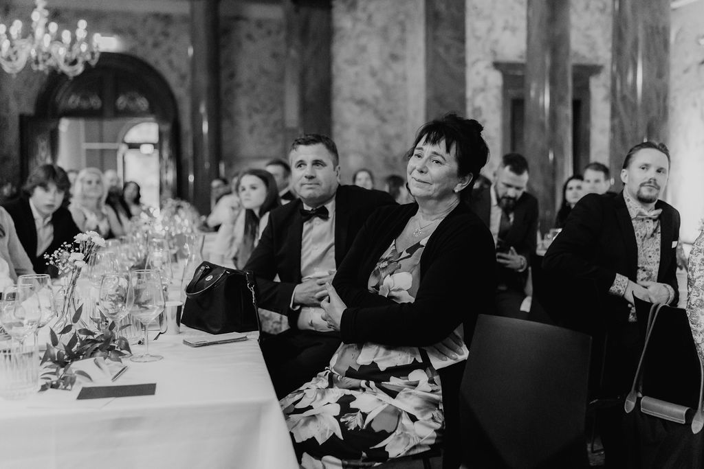 Wedding guest in floral dress smiles warmly during reception dinner in grand ballroom.