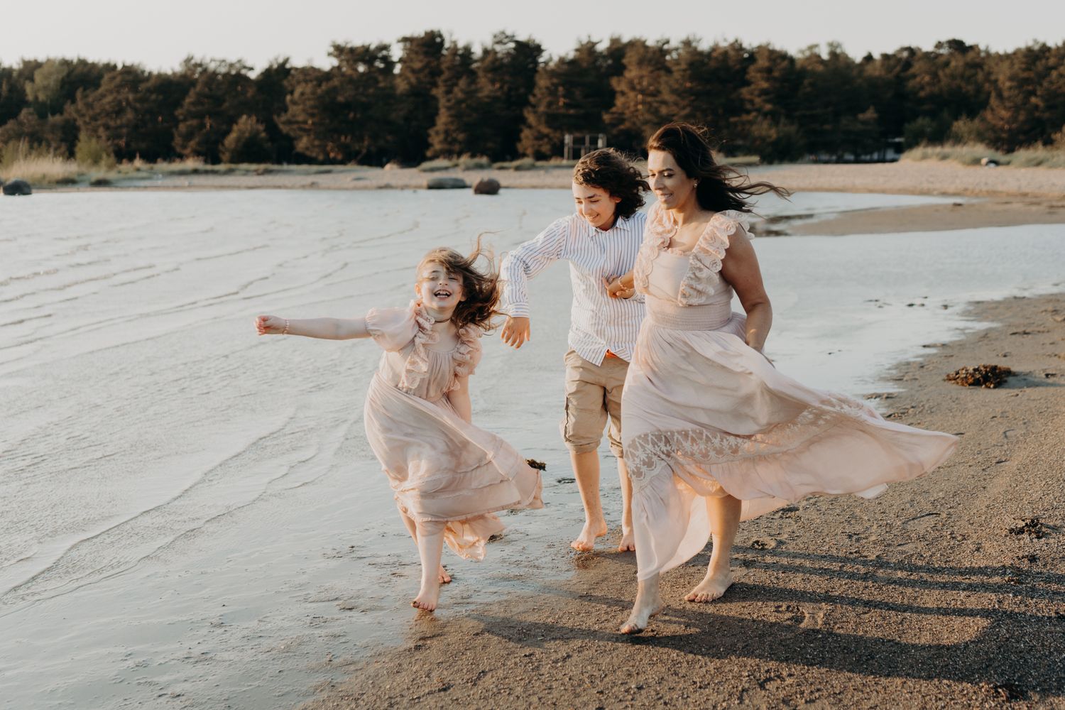 Joyful mother and two children running along a beach shoreline at golden hour.