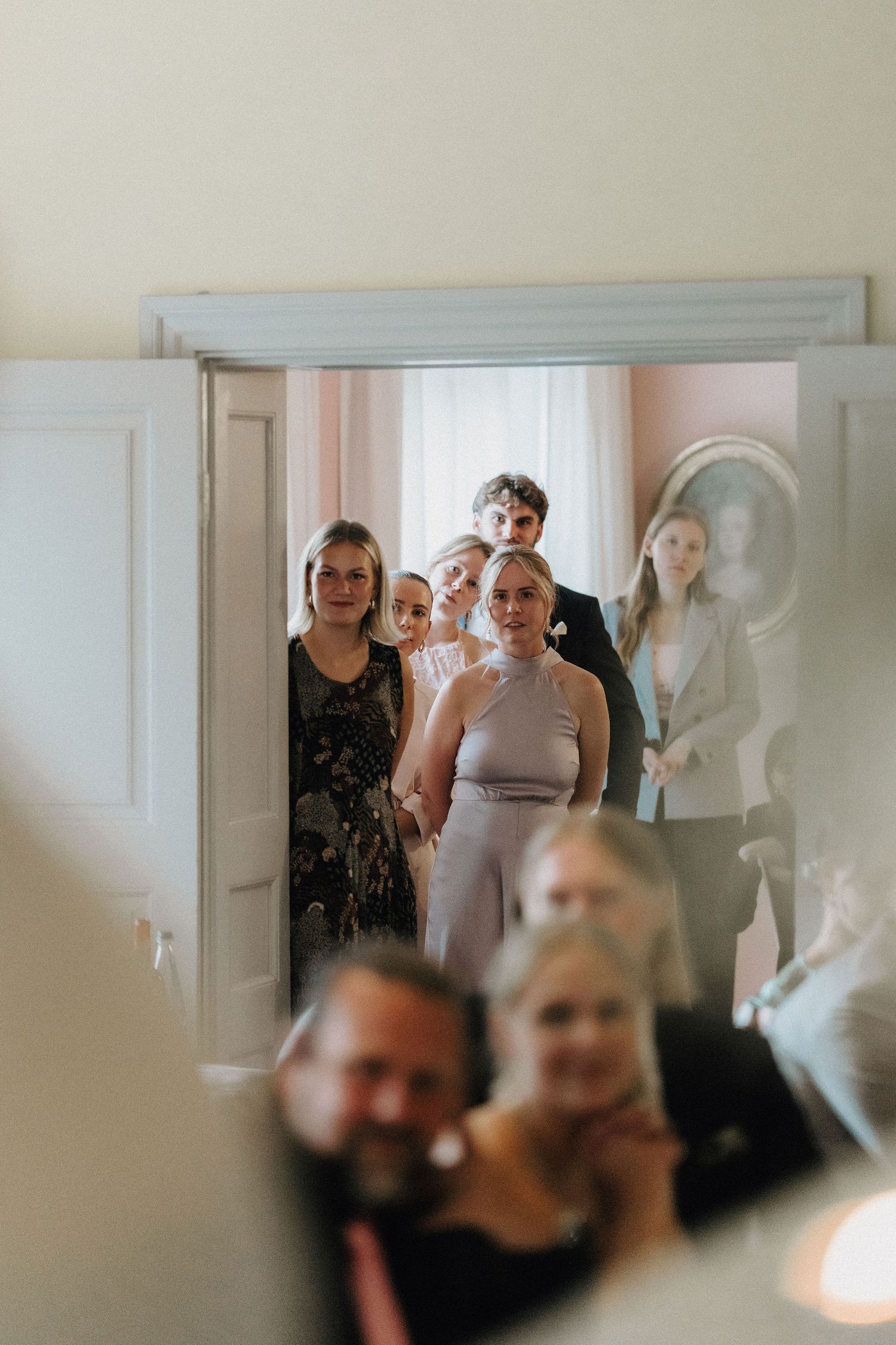 Wedding guests gathered in doorway watching reception proceedings in elegant decorated venue.
