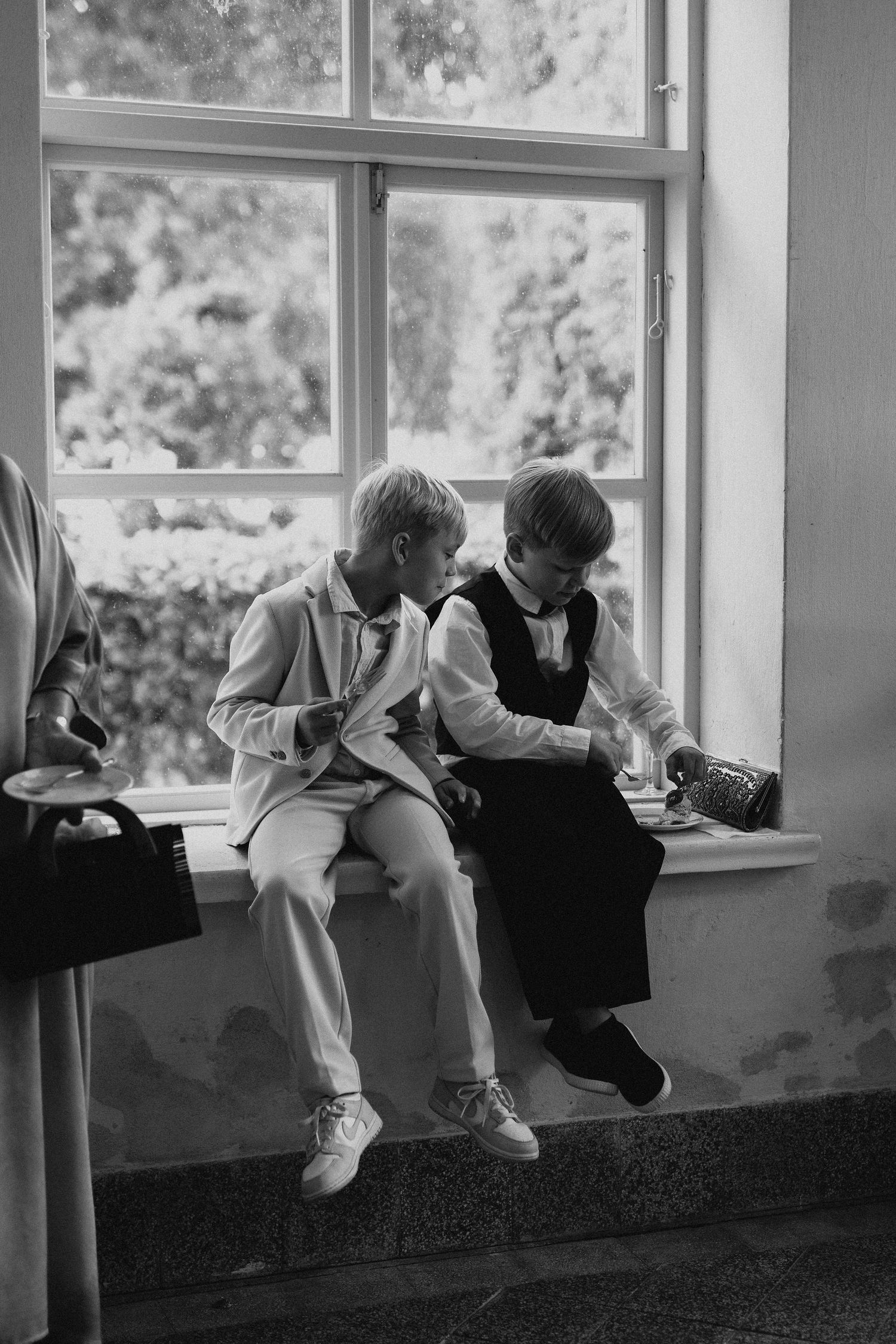 Black and white photo of two young boys sitting on windowsill at a wedding venue.