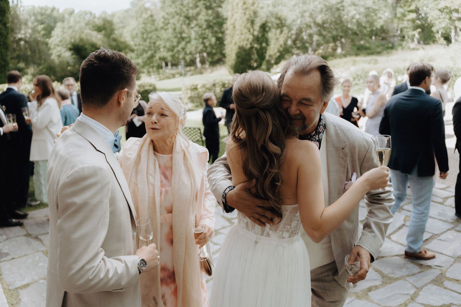 Bride and groom greet elderly guests with a warm embrace at their outdoor wedding reception.