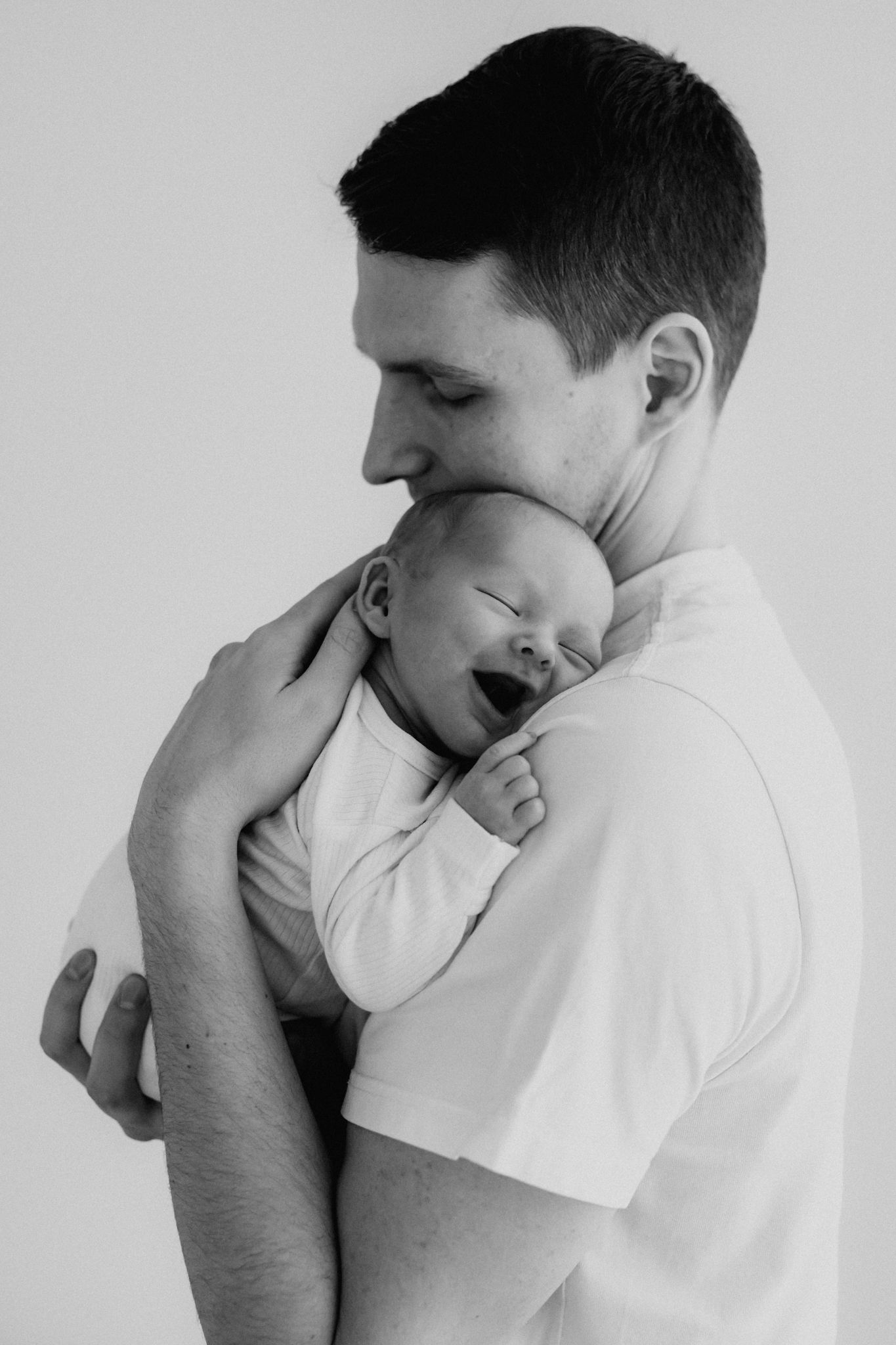 Black and white photo of a father tenderly holding his yawning newborn baby close to his chest.
