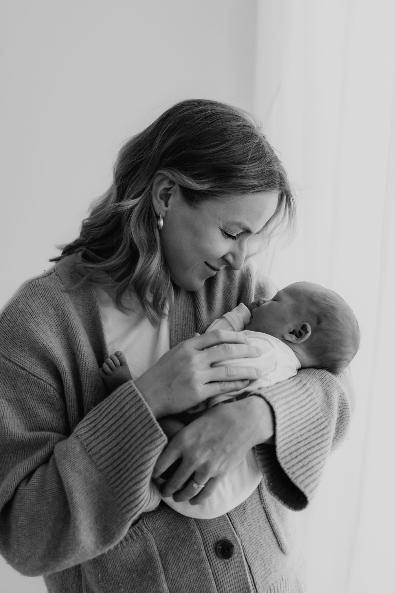 Black and white portrait of a smiling mother cradling her newborn baby close to her chest indoors.