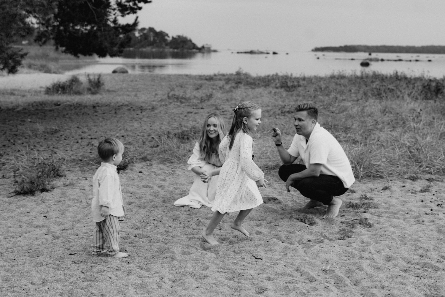A happy family with two children plays together on a sandy beach in a black and white photo.