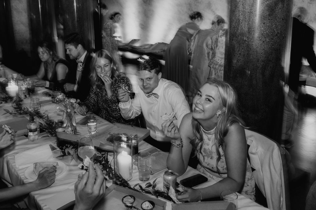 Black and white photo of wedding guests laughing and socializing at a decorated dinner table.