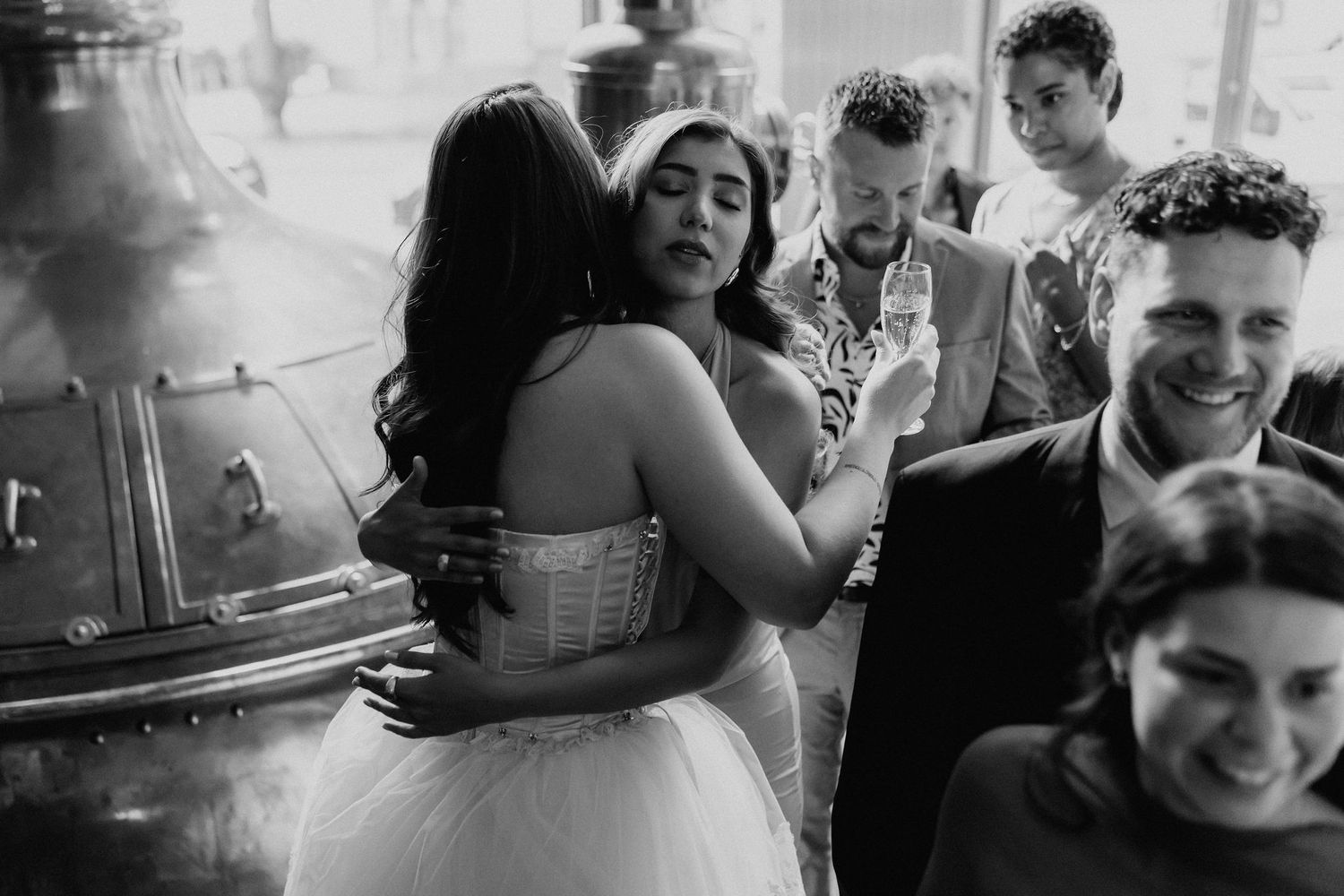 Black and white photo of bride embracing a guest at a lively wedding reception celebration.