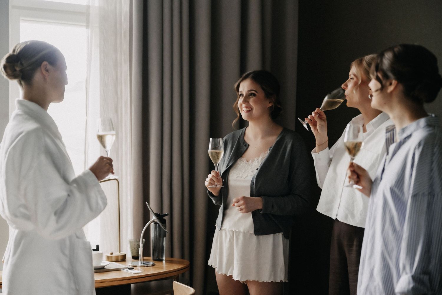 Bridesmaids in robes and elegant attire toasting with champagne glasses during a bridal party getting ready celebration.