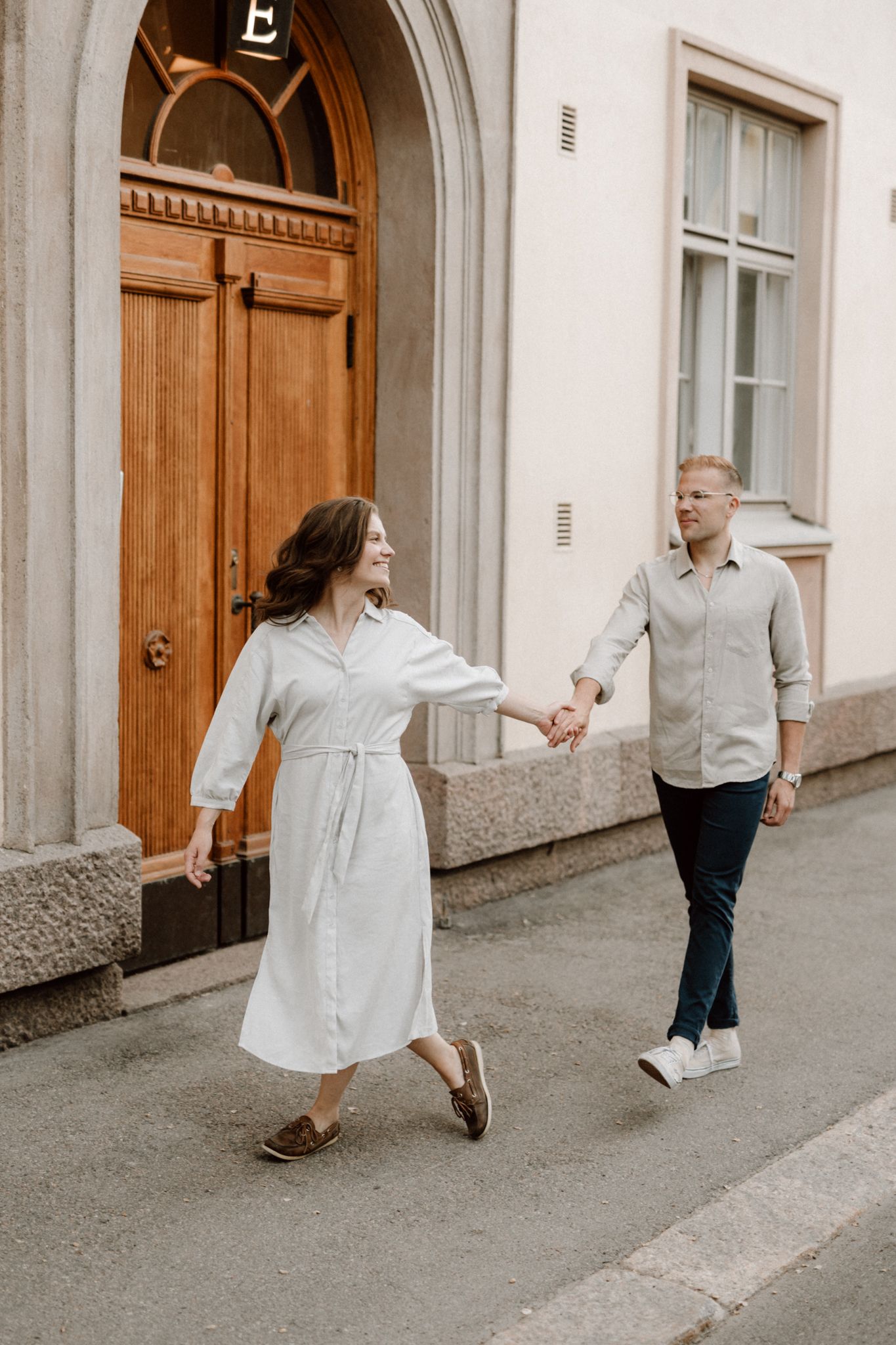 Couple holding hands walking along a cobblestone street near a classic arched wooden door.