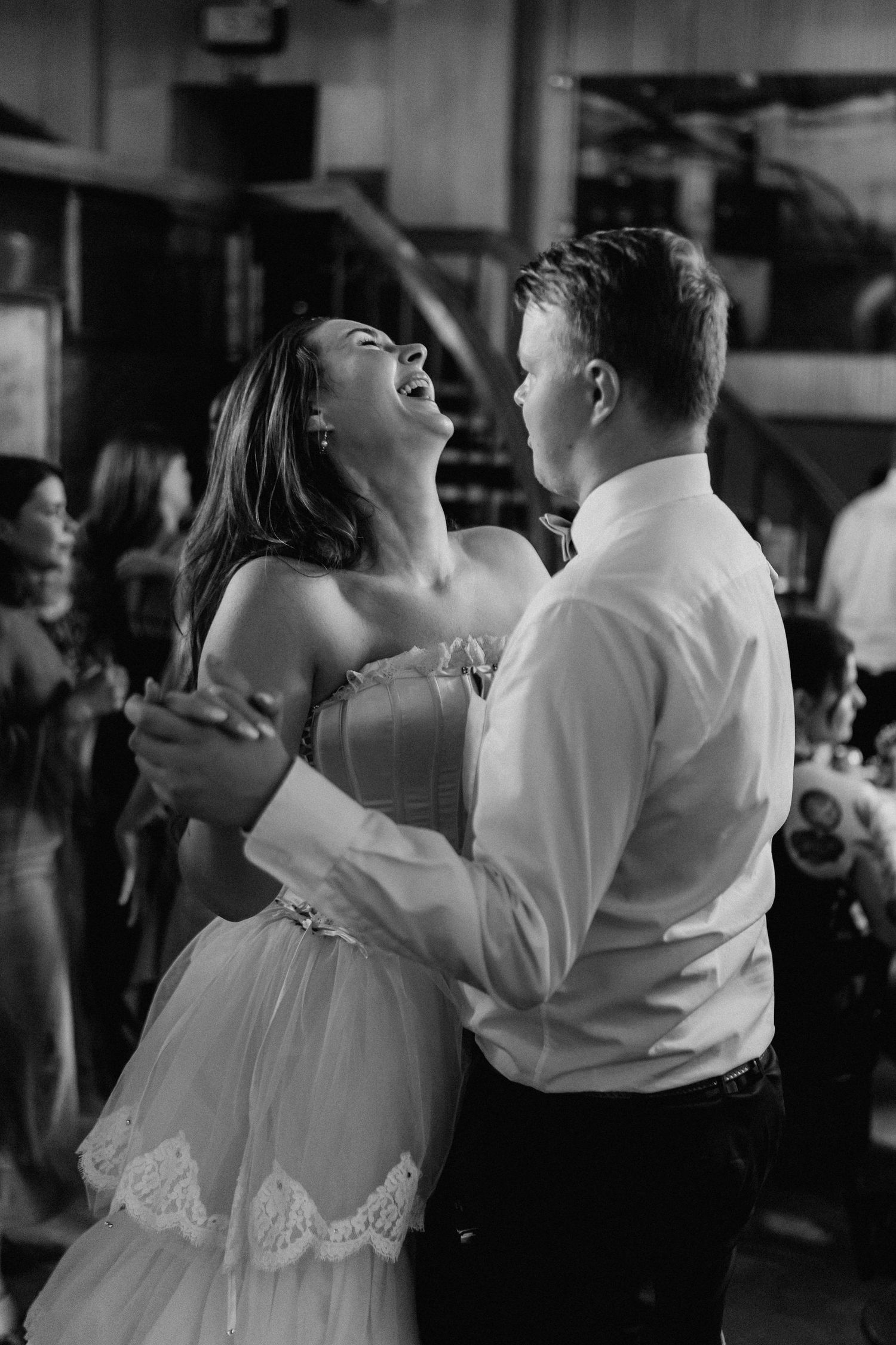 Bride laughs joyfully while dancing with partner at wedding reception in black and white.