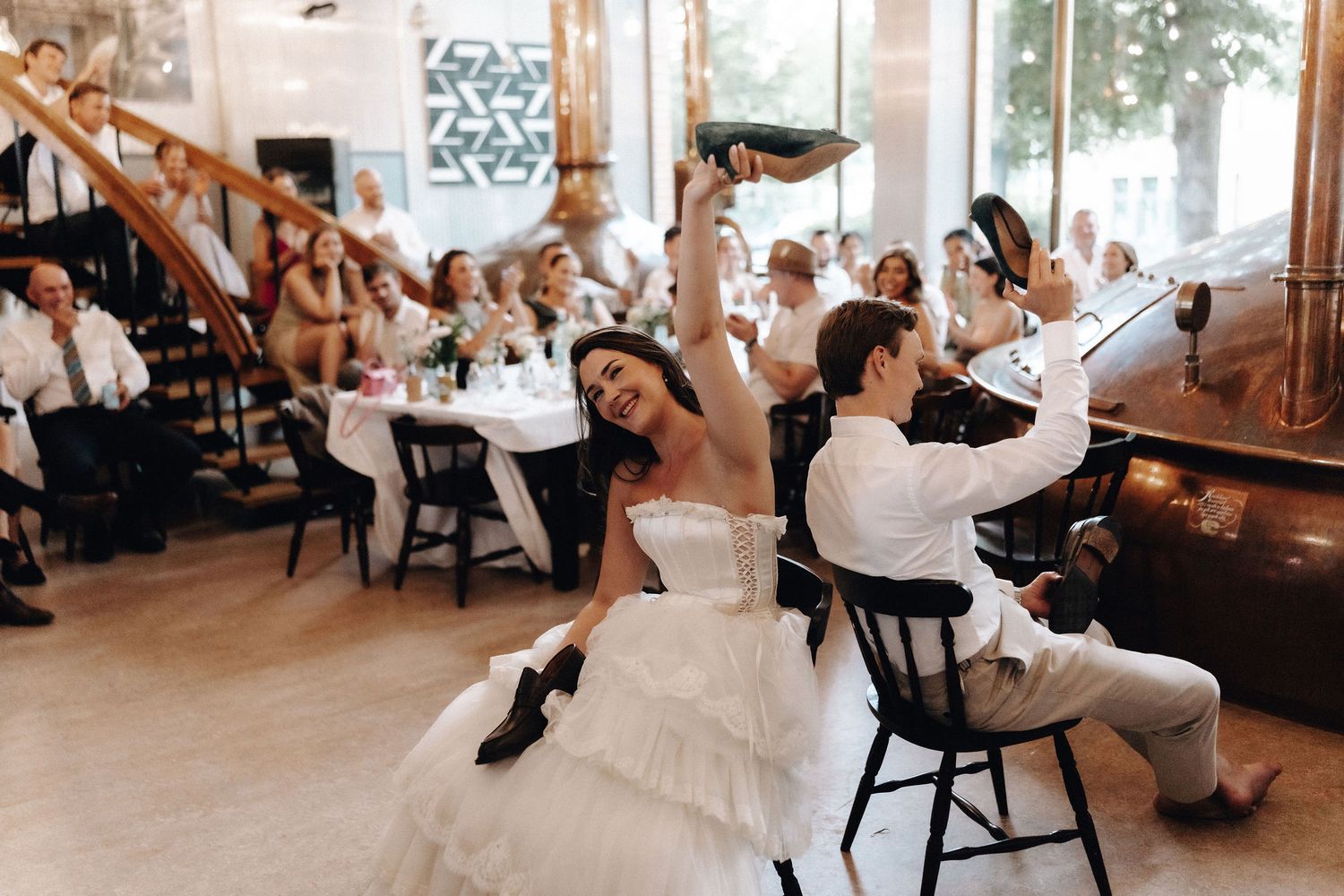 Bride and groom celebrate joyfully with raised shoes at wedding reception.