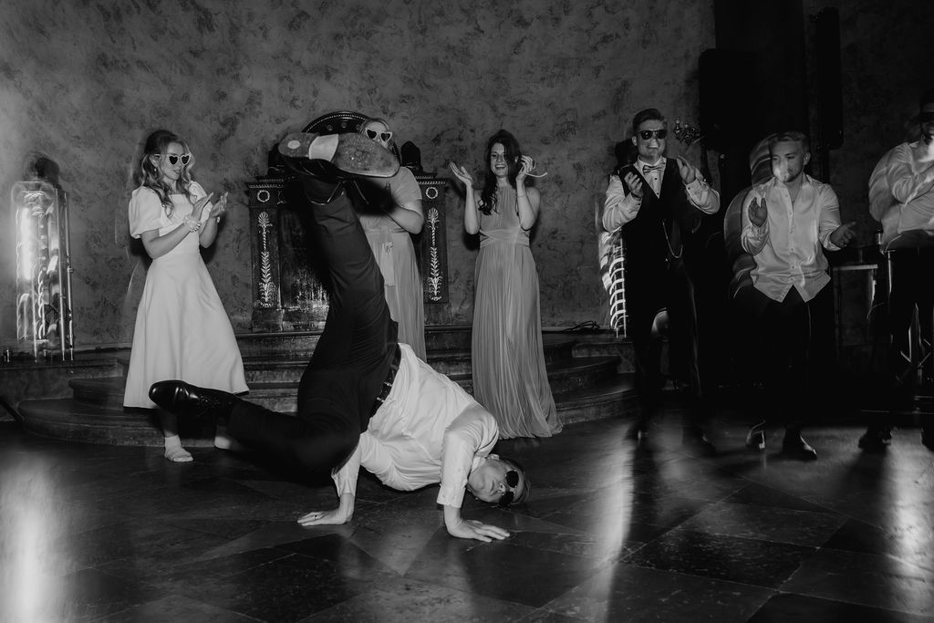Black and white photo of groomsman breakdancing while wedding guests cheer at reception.