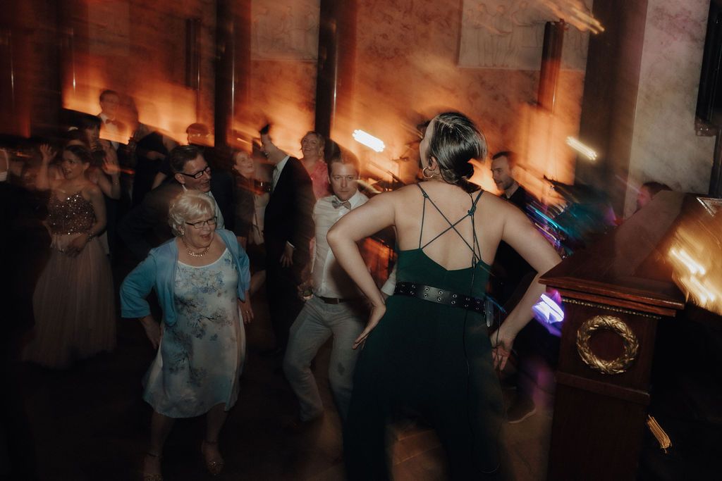 Wedding guests dancing energetically in a warmly lit venue with a woman in a green dress.