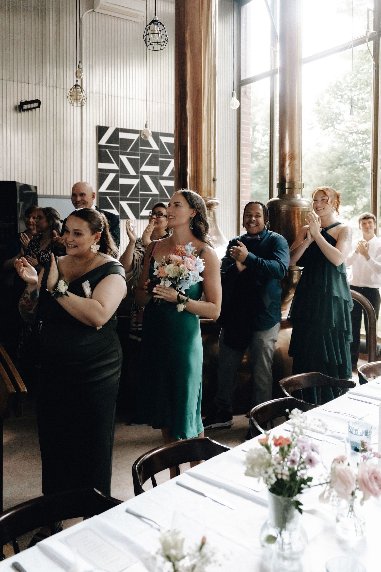 Bridesmaids in emerald green dresses clap and cheer as couple arrives at elegant wedding reception.
