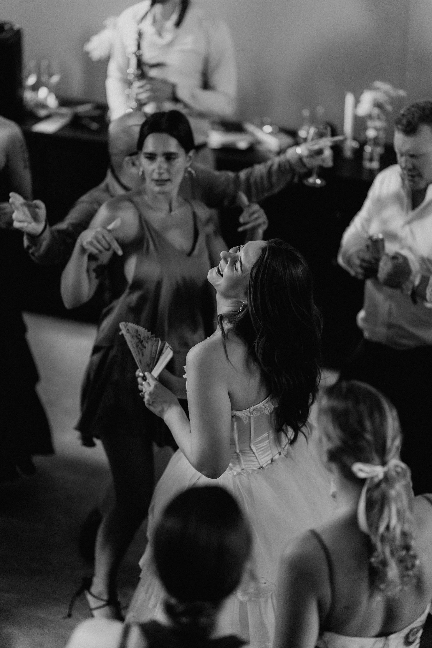 Bride laughs joyfully while dancing with guests at wedding reception.