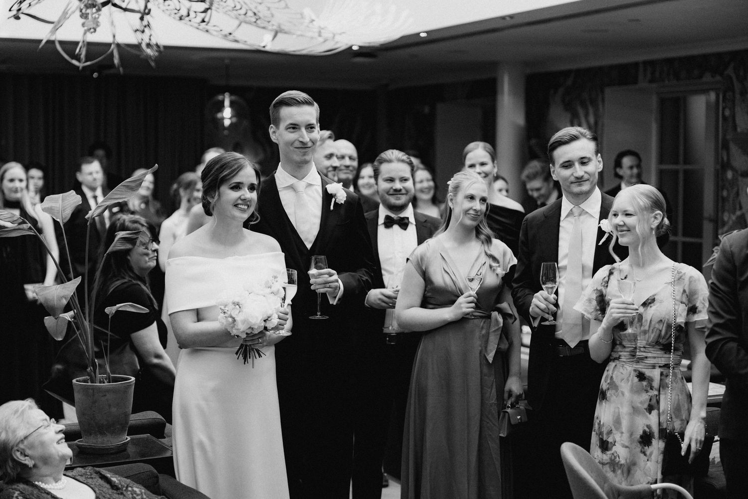 Bride and groom pose with wedding guests holding champagne glasses at an elegant black and white reception.
