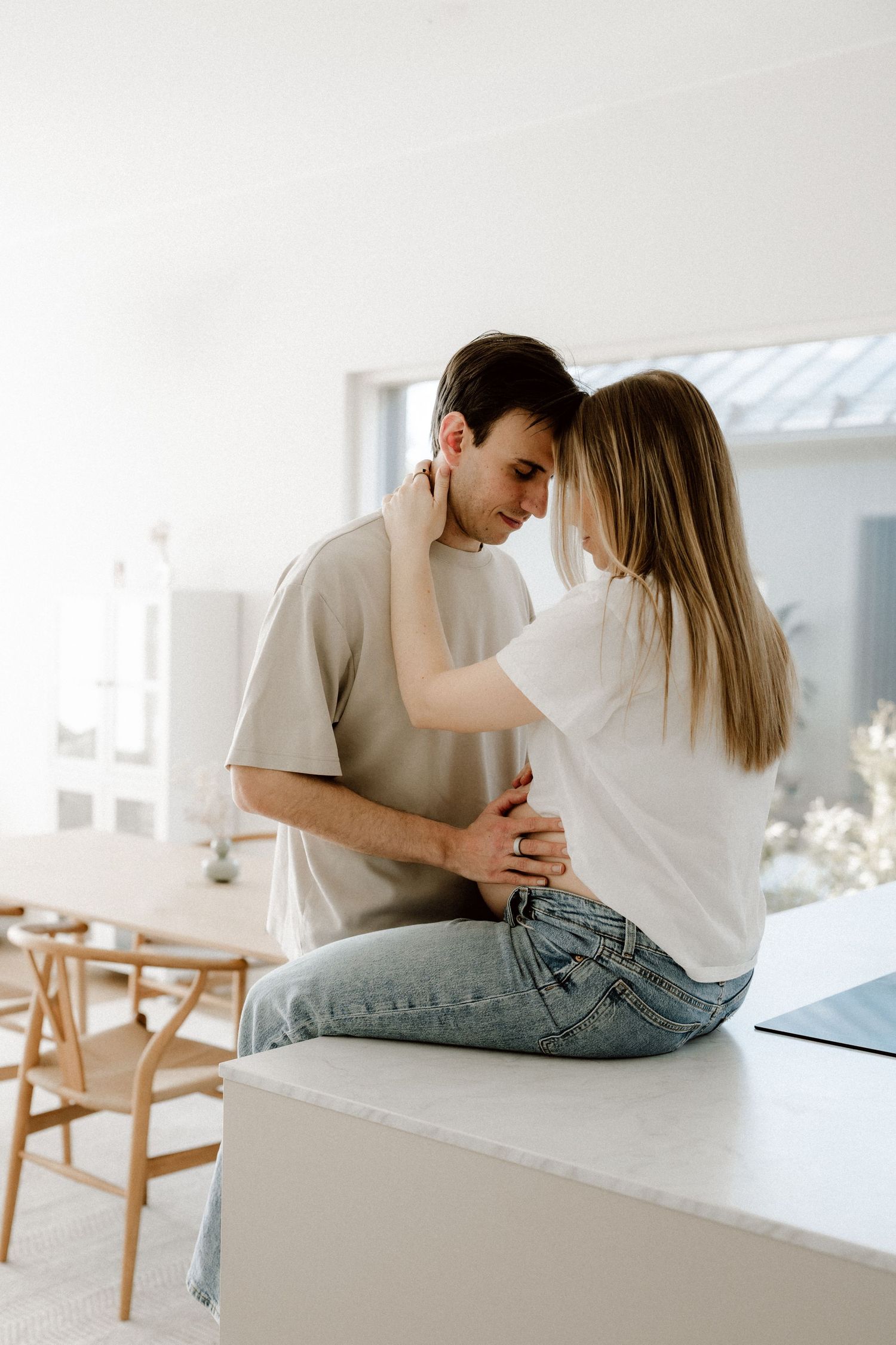 Romantic couple sharing an intimate moment, woman sitting on white counter embracing man in cozy modern home.