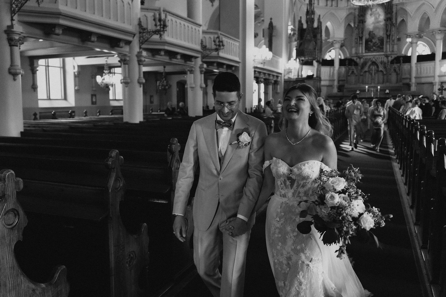 Black and white photo of bride and groom walking down church aisle after ceremony.