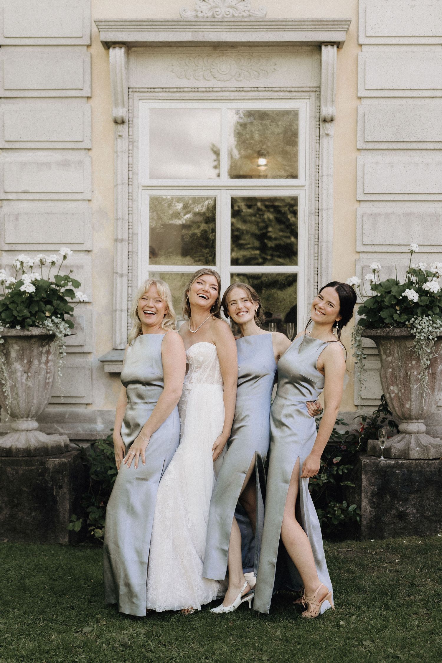Bride in strapless white gown smiling with three bridesmaids in light blue satin dresses outside.