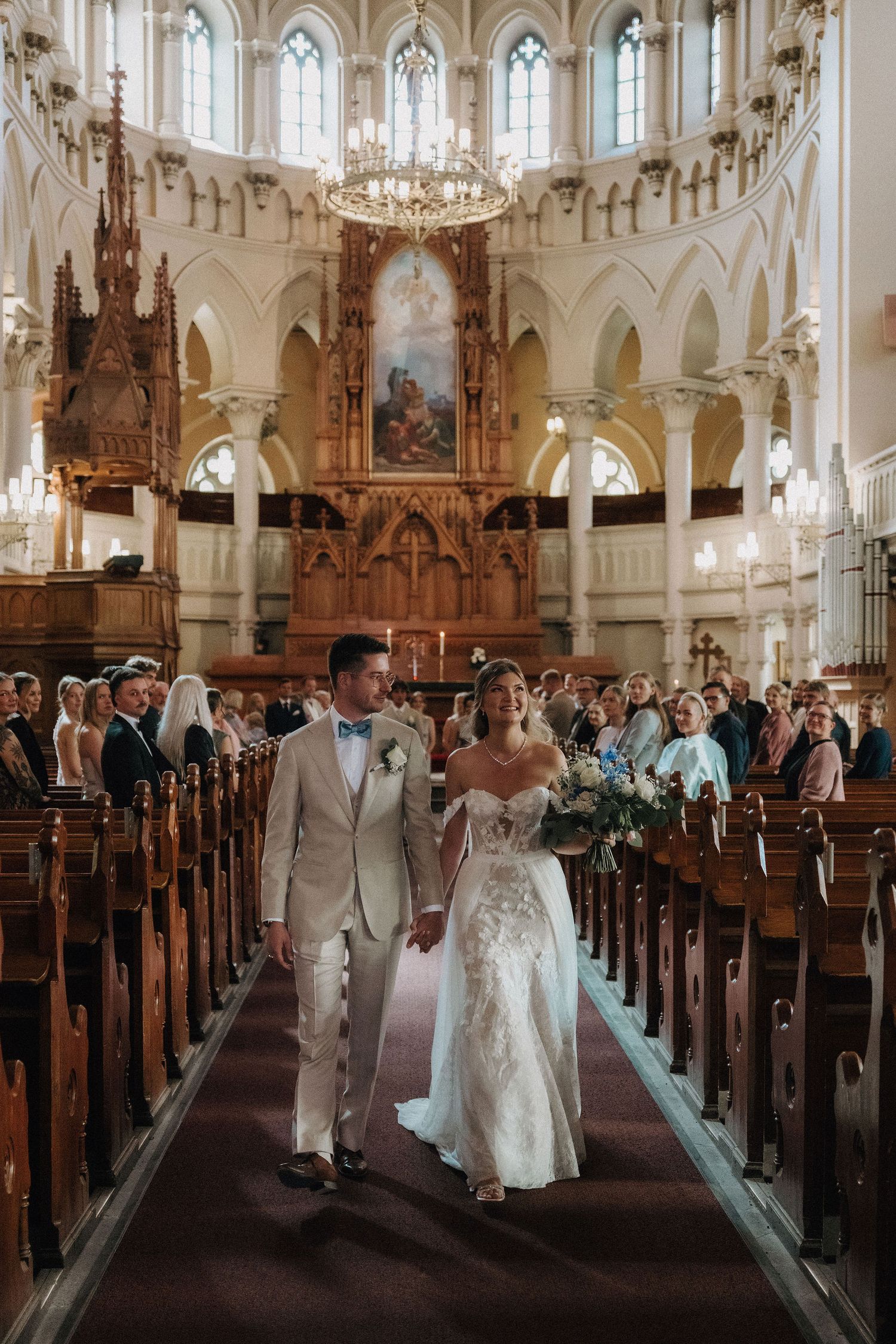 Newlyweds walk hand-in-hand down grand church aisle after wedding ceremony.