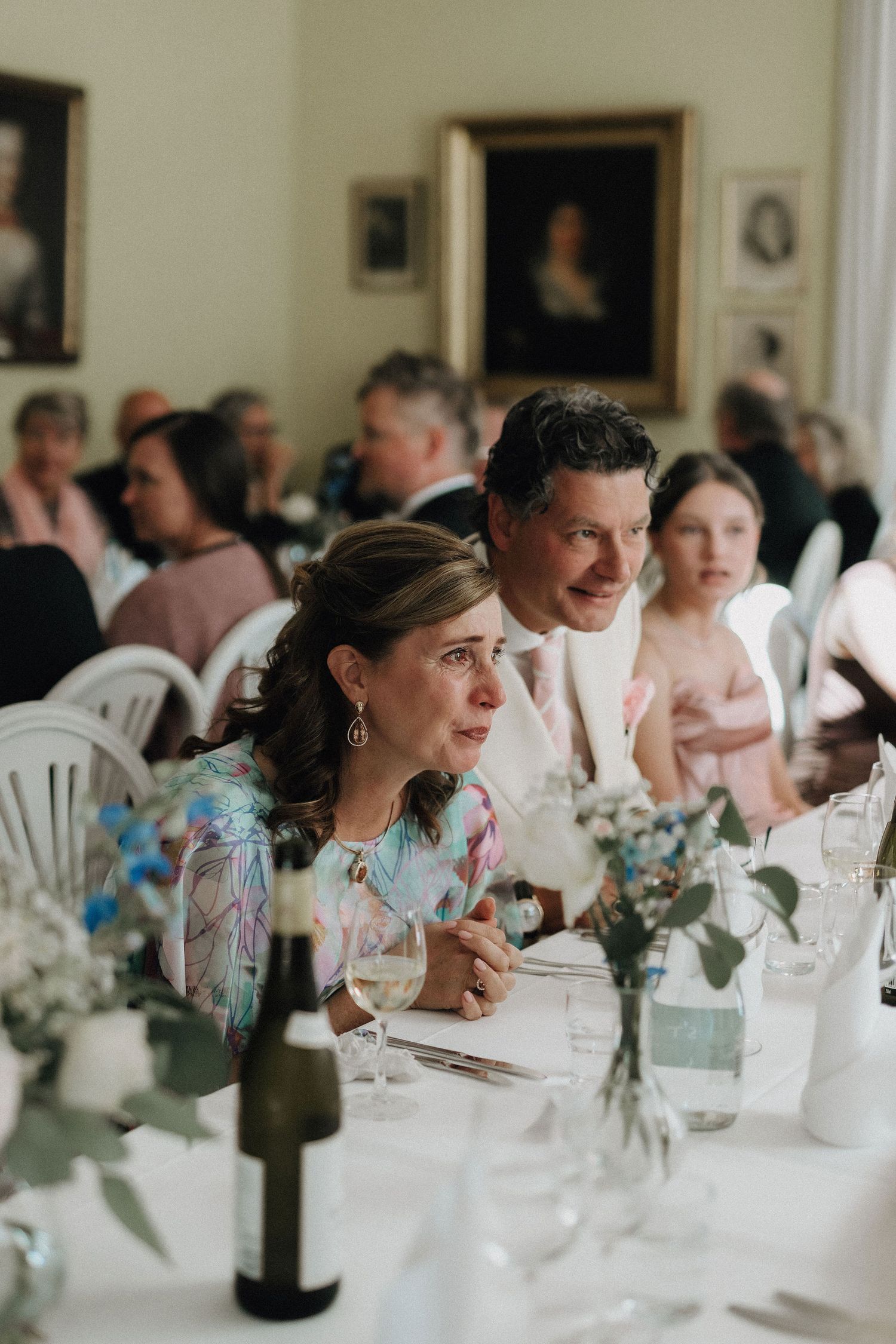 Wedding guests attentively watch ceremony at elegantly decorated table with blue floral arrangements.