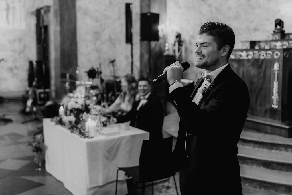 Black and white photo of a man giving a heartfelt speech with a microphone at the wedding.