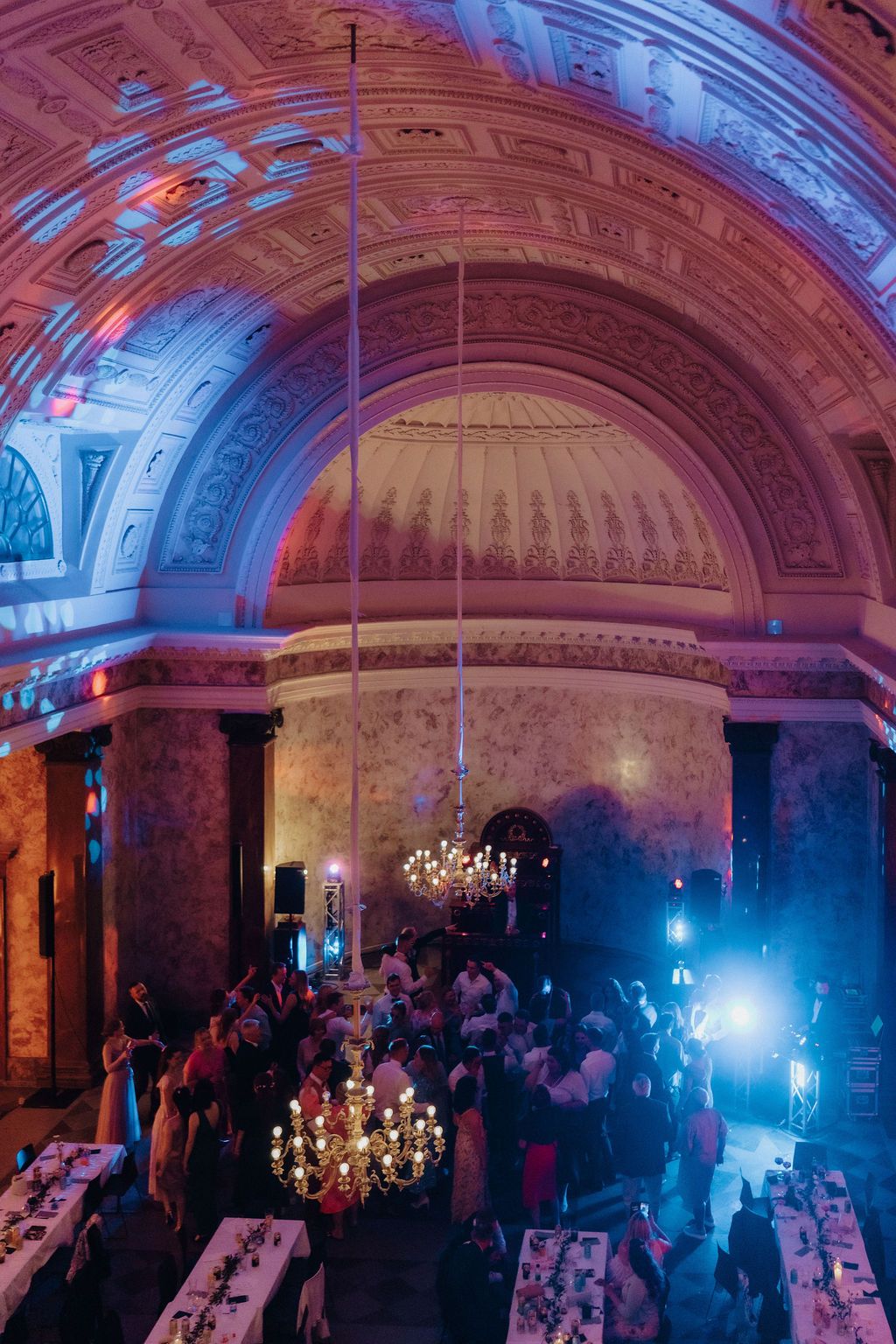 Aerial view of elegant wedding reception in grand vaulted hall with colorful uplighting and chandelier.