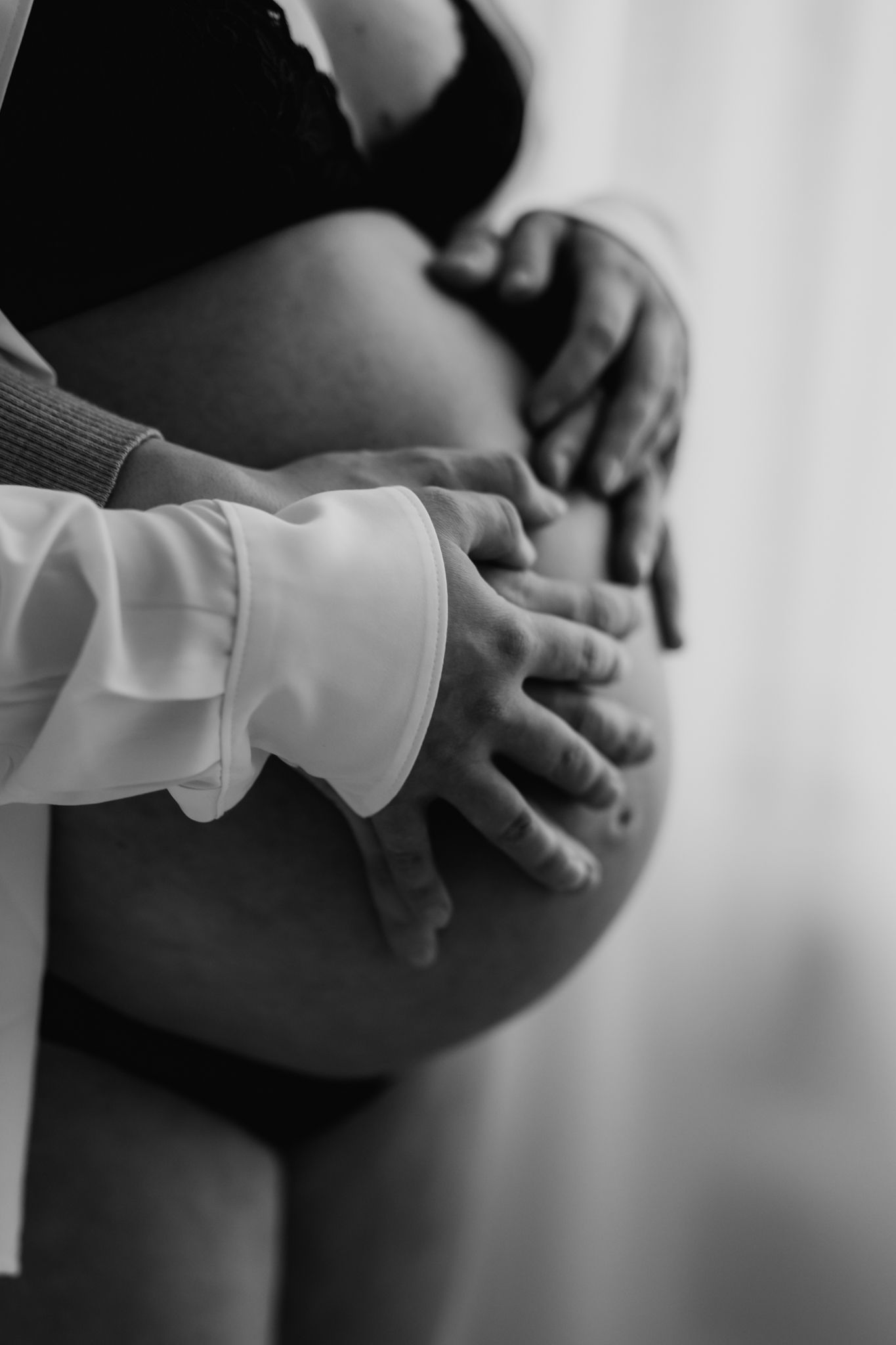 Close-up black and white image of couple's hands tenderly holding pregnant woman's bare belly.