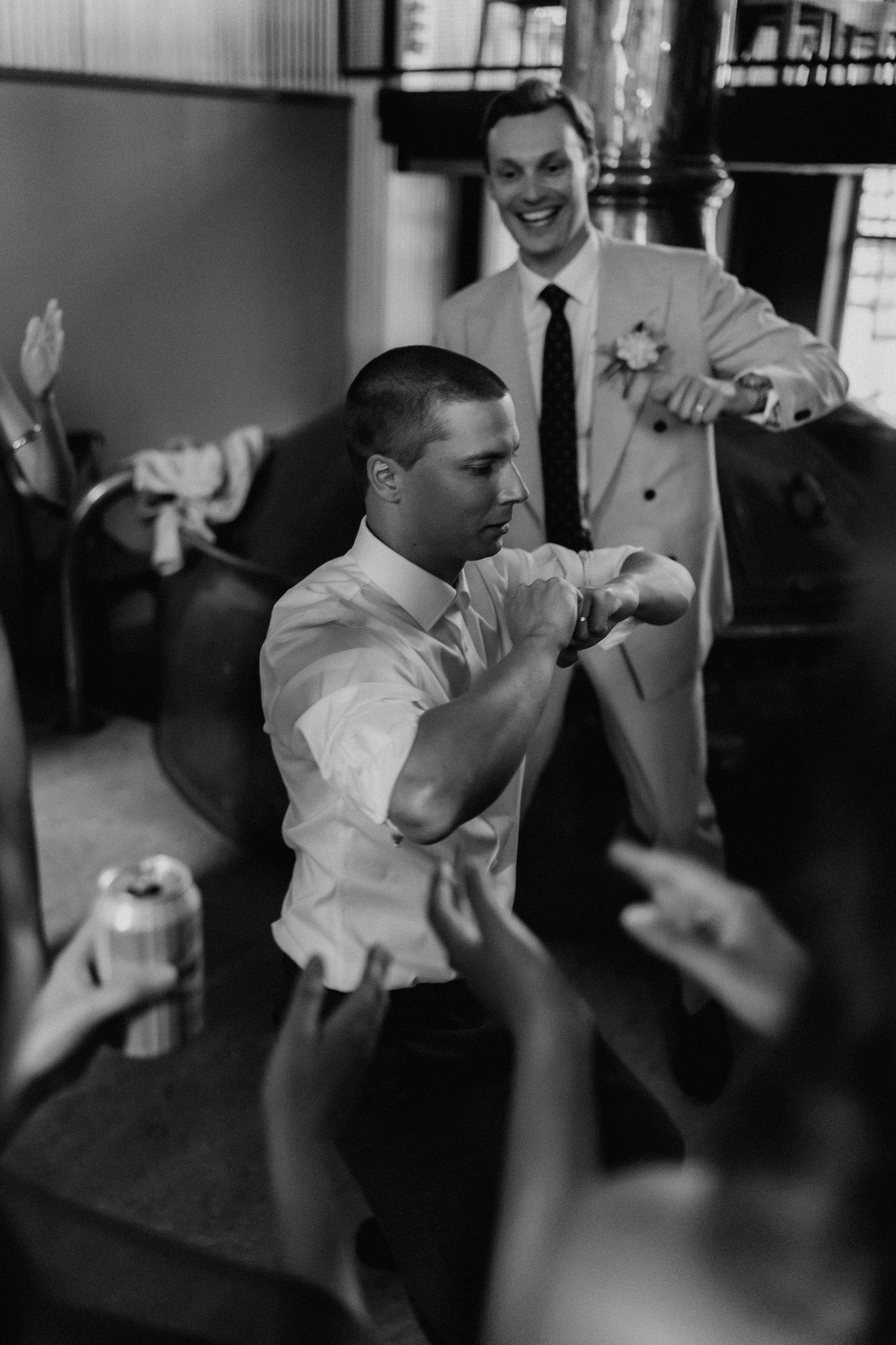 Groomsman shows off dance moves while friends cheer at wedding reception in black and white.