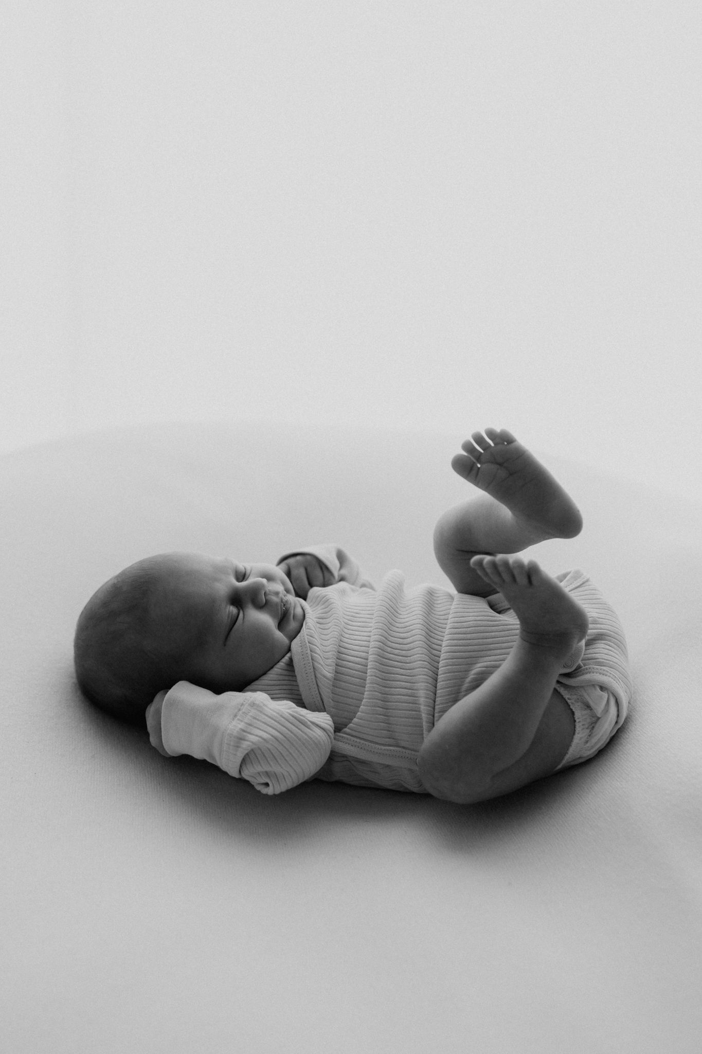 Black and white photo of newborn baby lying on back with feet raised.