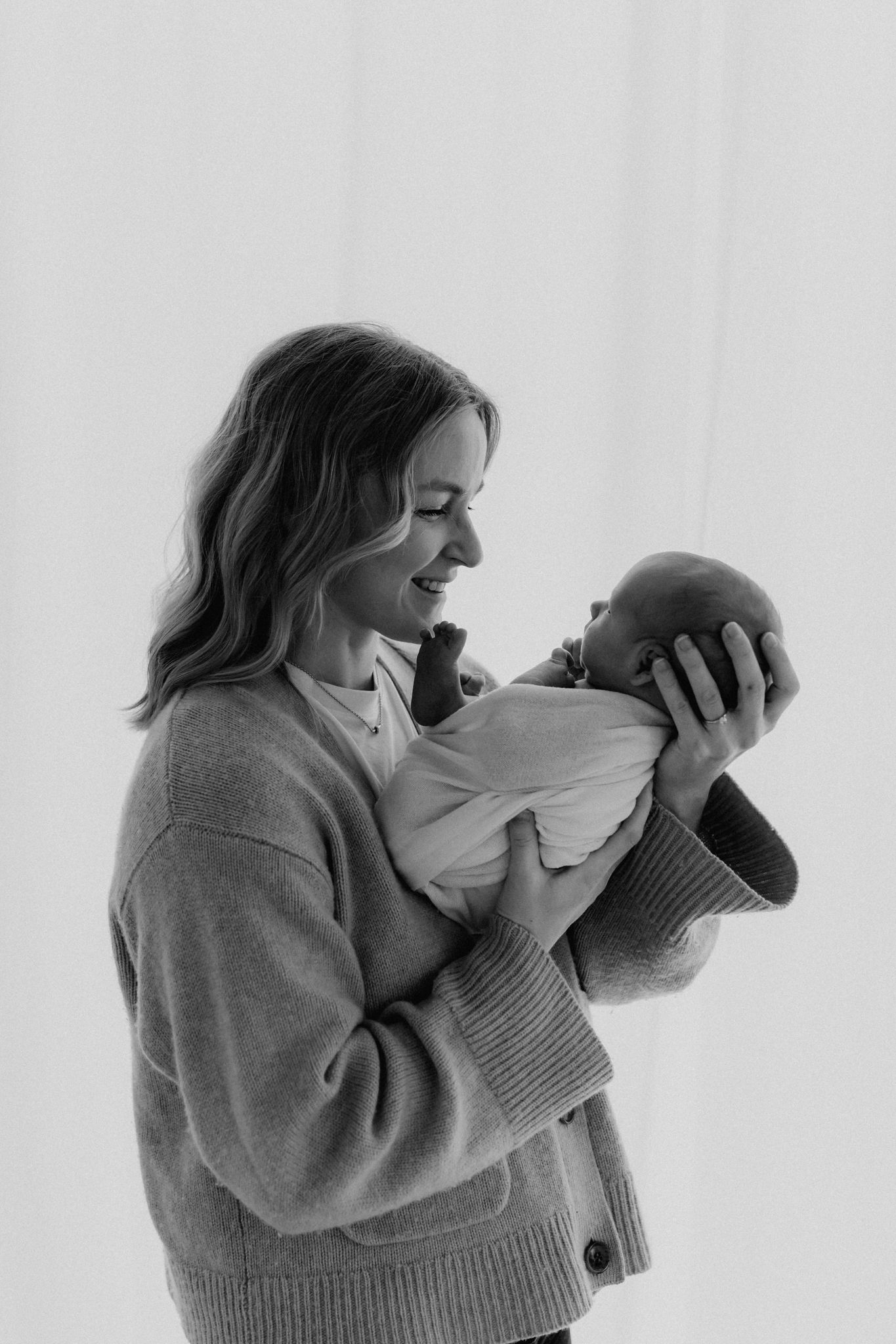 Black and white photo of a joyful mother smiling at her newborn baby held in her arms.