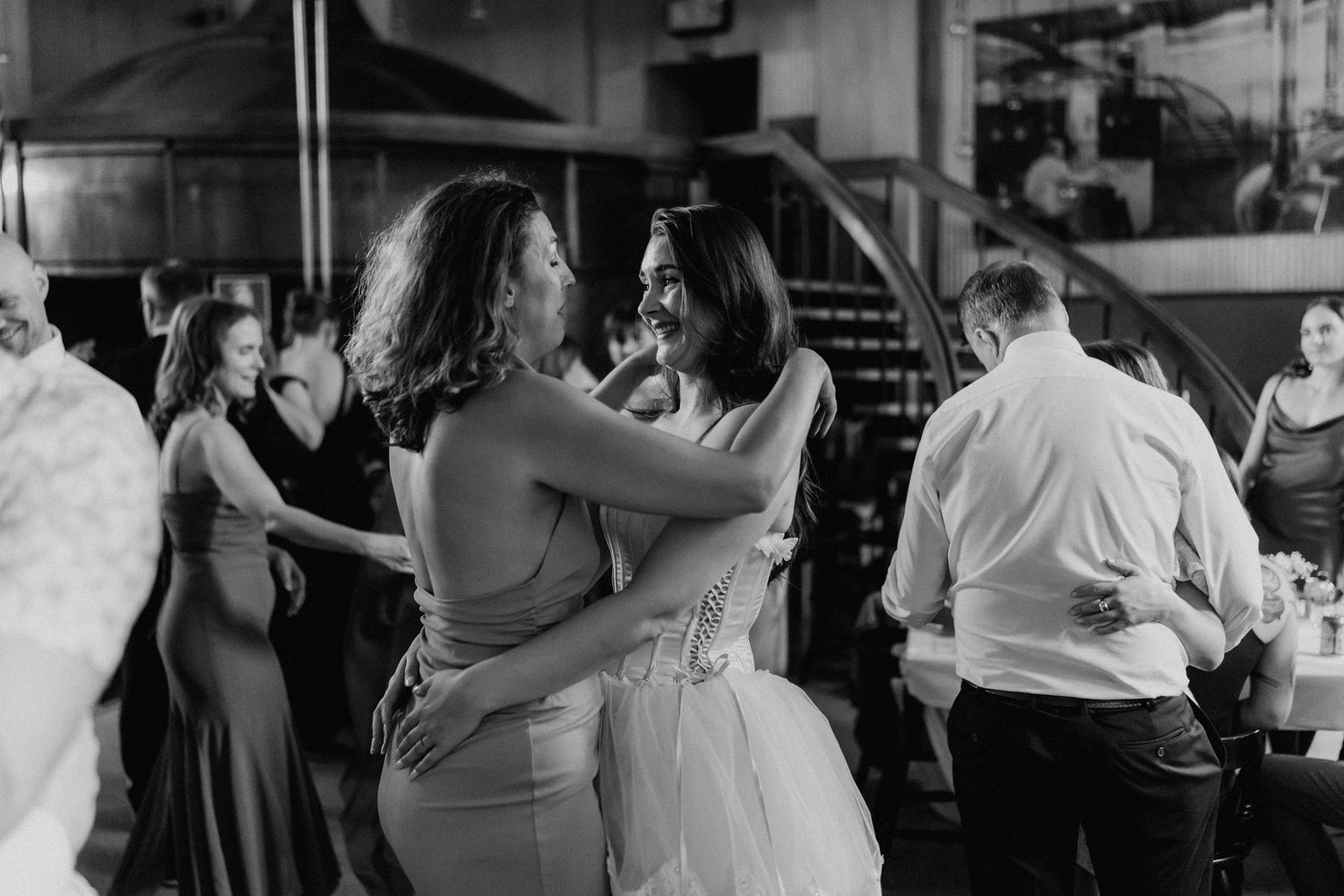 Two women share an emotional dance embrace at a wedding reception in black and white.