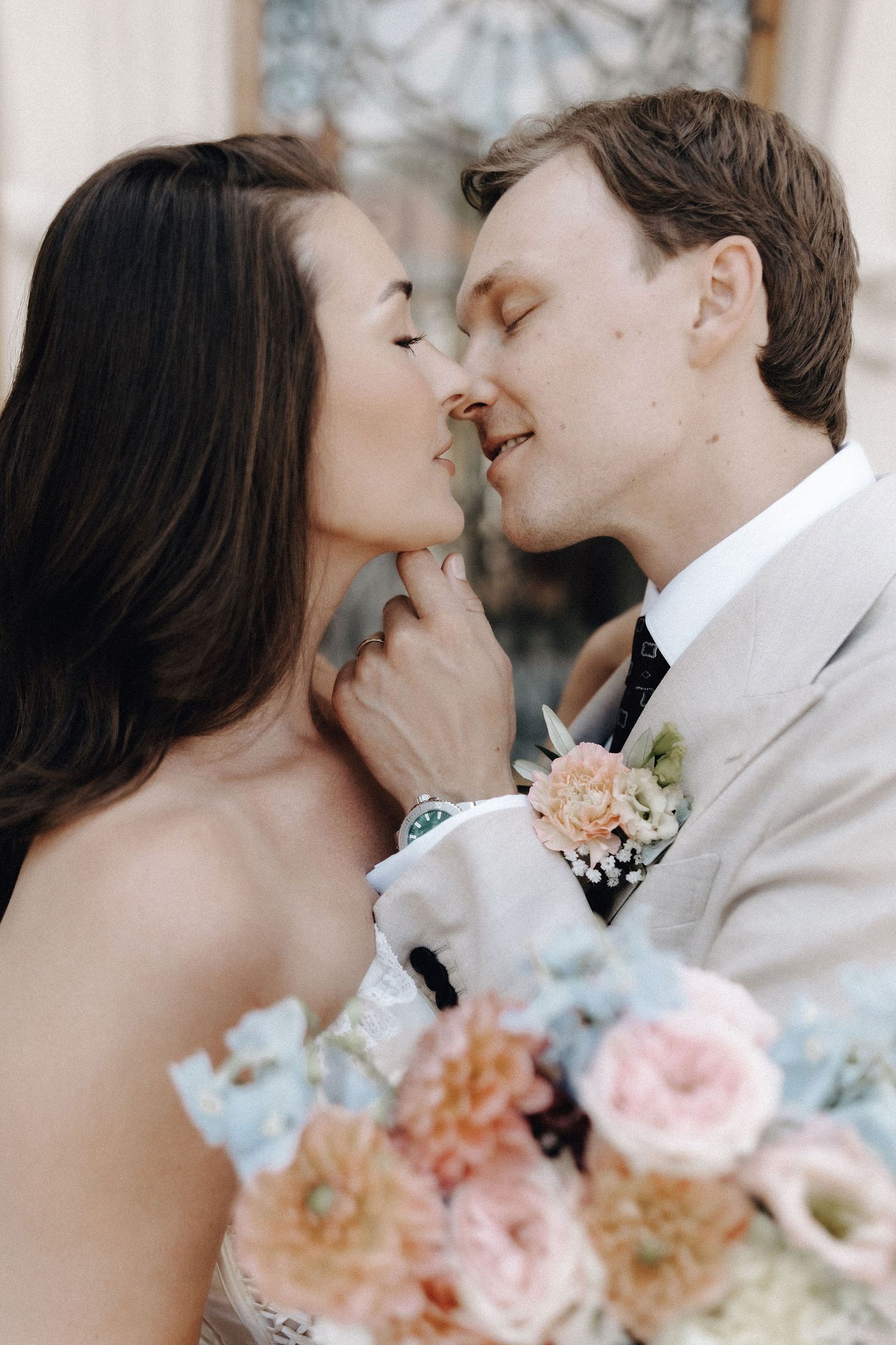 Close-up of bride and groom about to kiss, holding a pastel floral bouquet of roses and blooms.