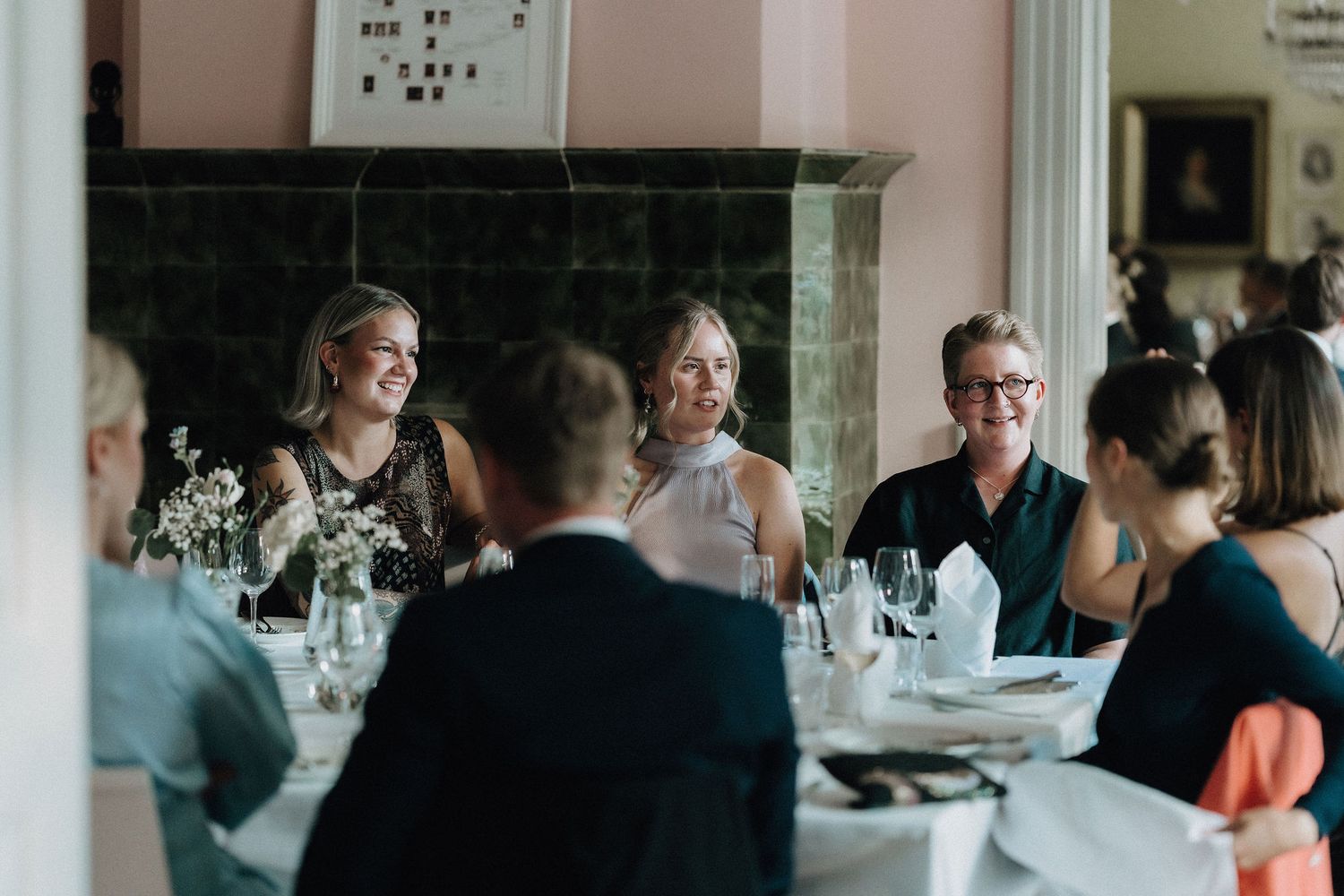 Group of smiling women in formal attire enjoying conversation at a wedding reception dinner table.