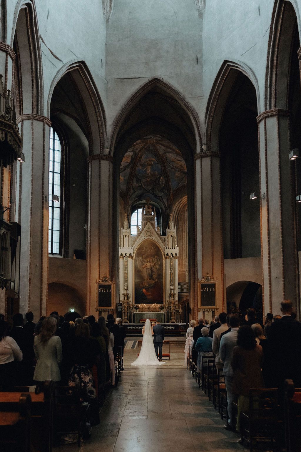 Wide view of bride and groom at altar of grand Gothic church during wedding ceremony.