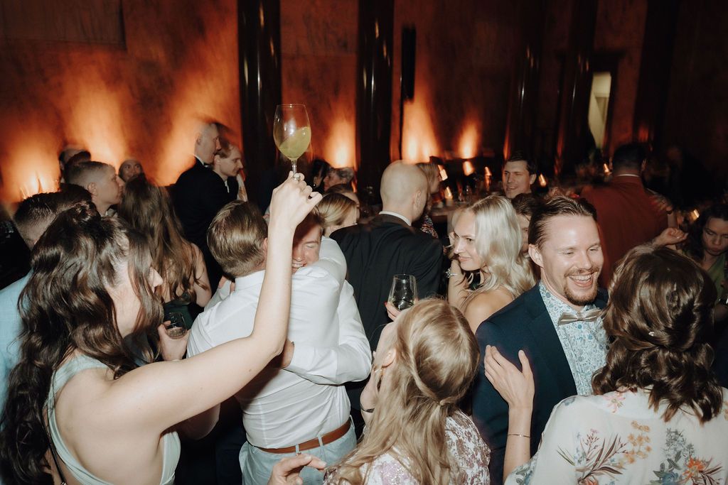 Wedding guests laugh and celebrate with drinks on a lively reception dance floor.