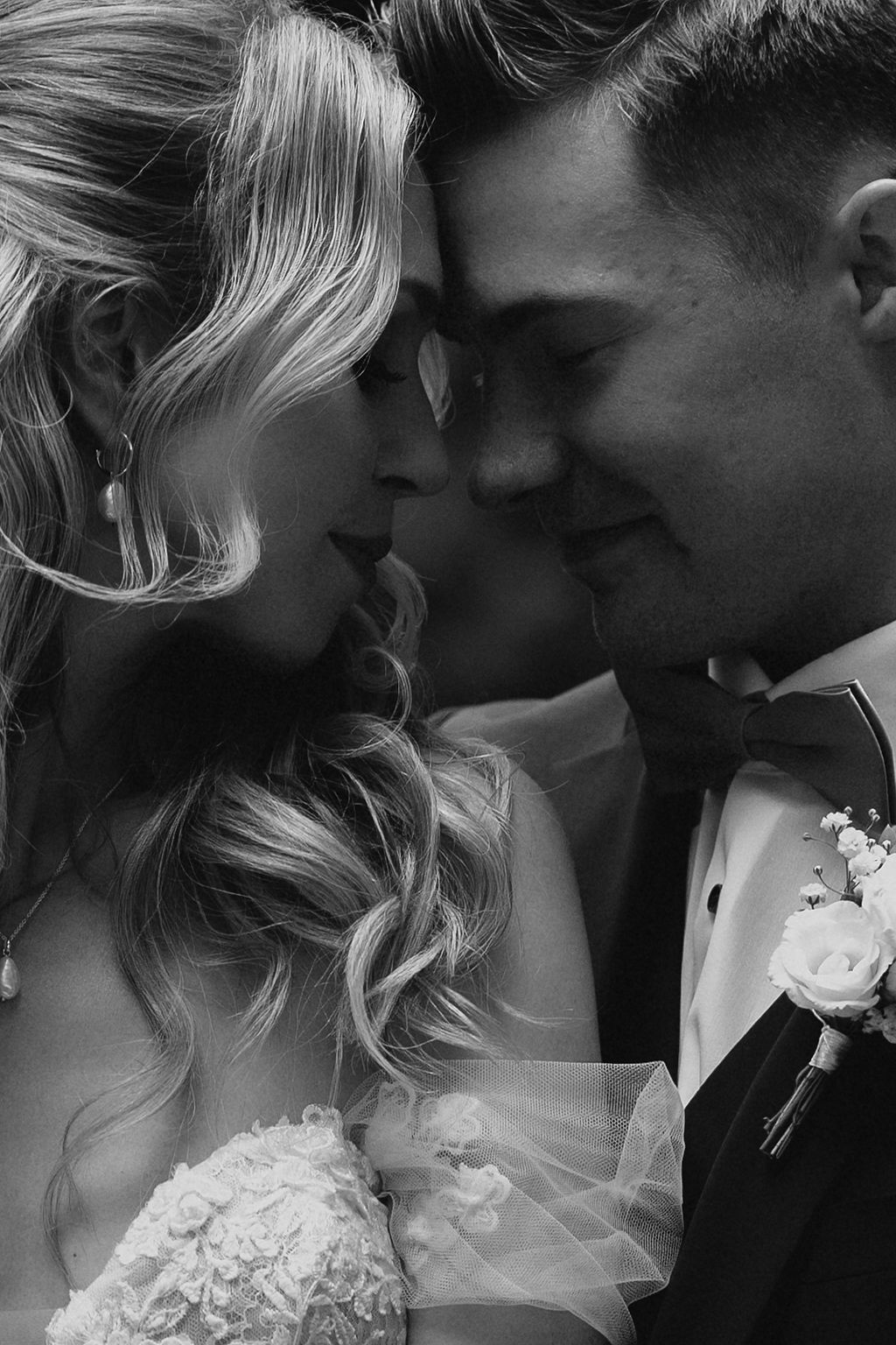 Intimate black and white close-up of bride and groom touching foreheads, smiling tenderly on wedding day.