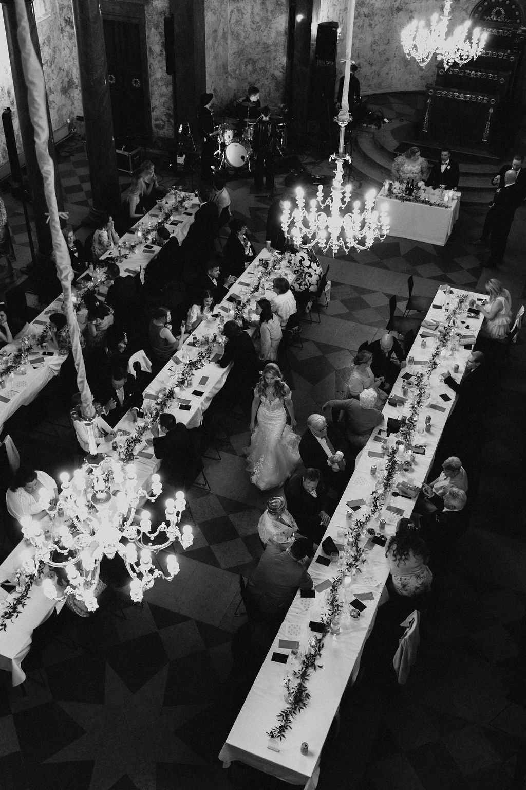 Aerial black and white view of elegant wedding reception inside grand hall with chandeliers and long tables.