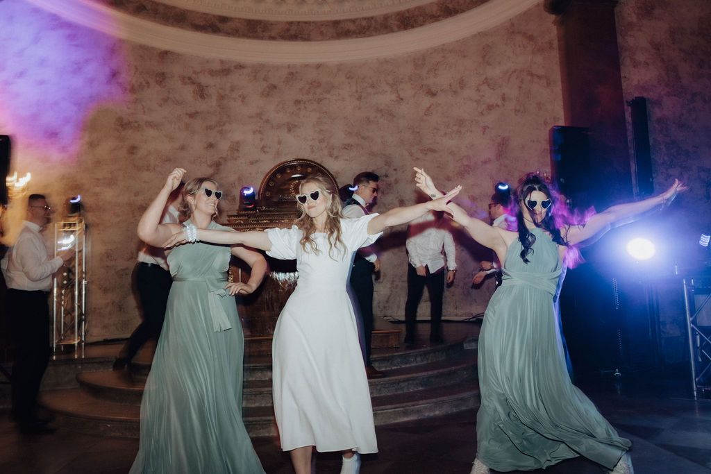 Bridesmaids in mint green dresses and sunglasses dancing joyfully at a wedding reception.