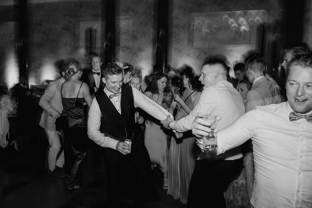 Energetic black and white photo of male wedding guests dancing at reception.