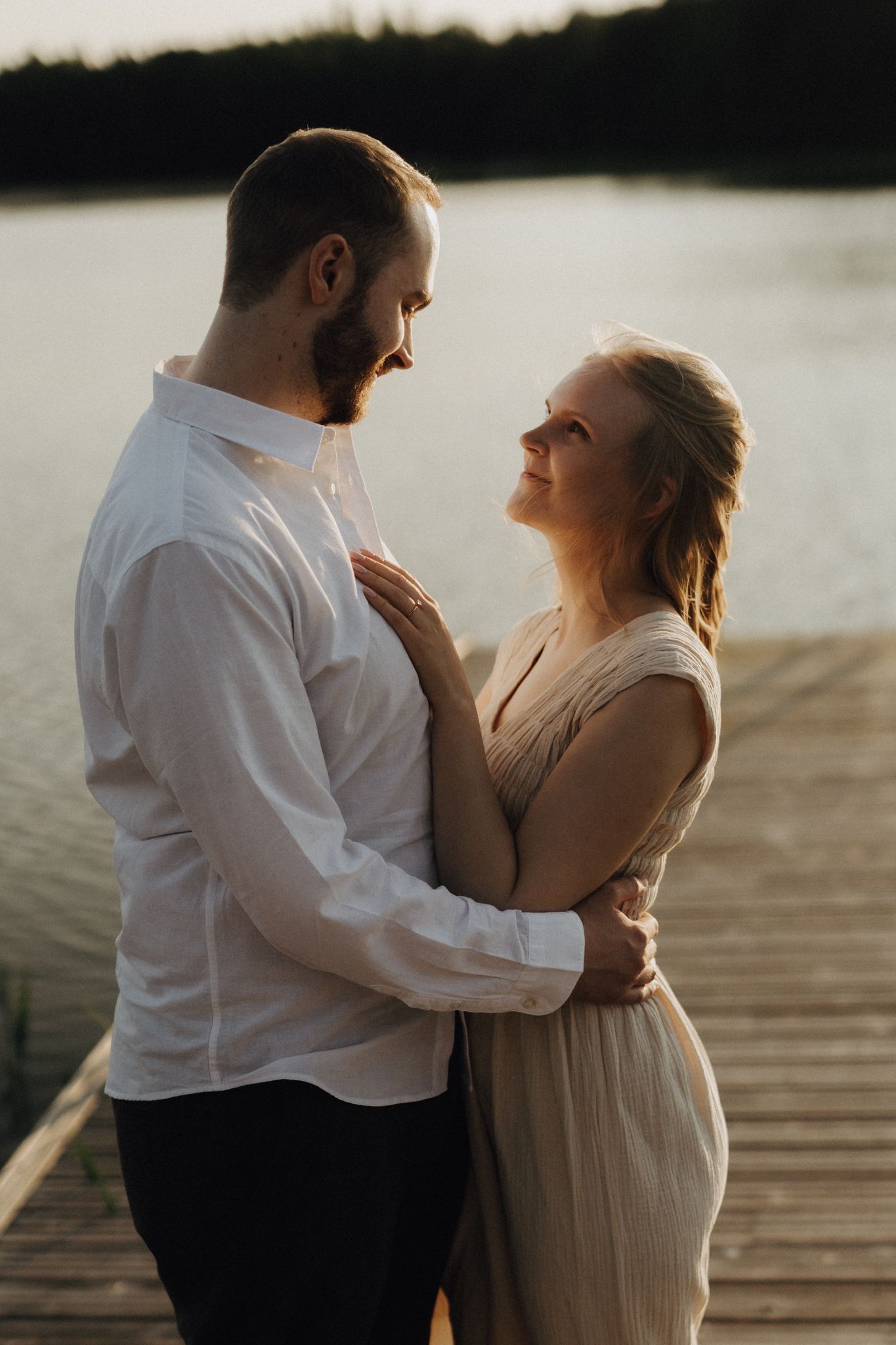 Couple embracing on a wooden dock at golden hour with a serene lake in the background.