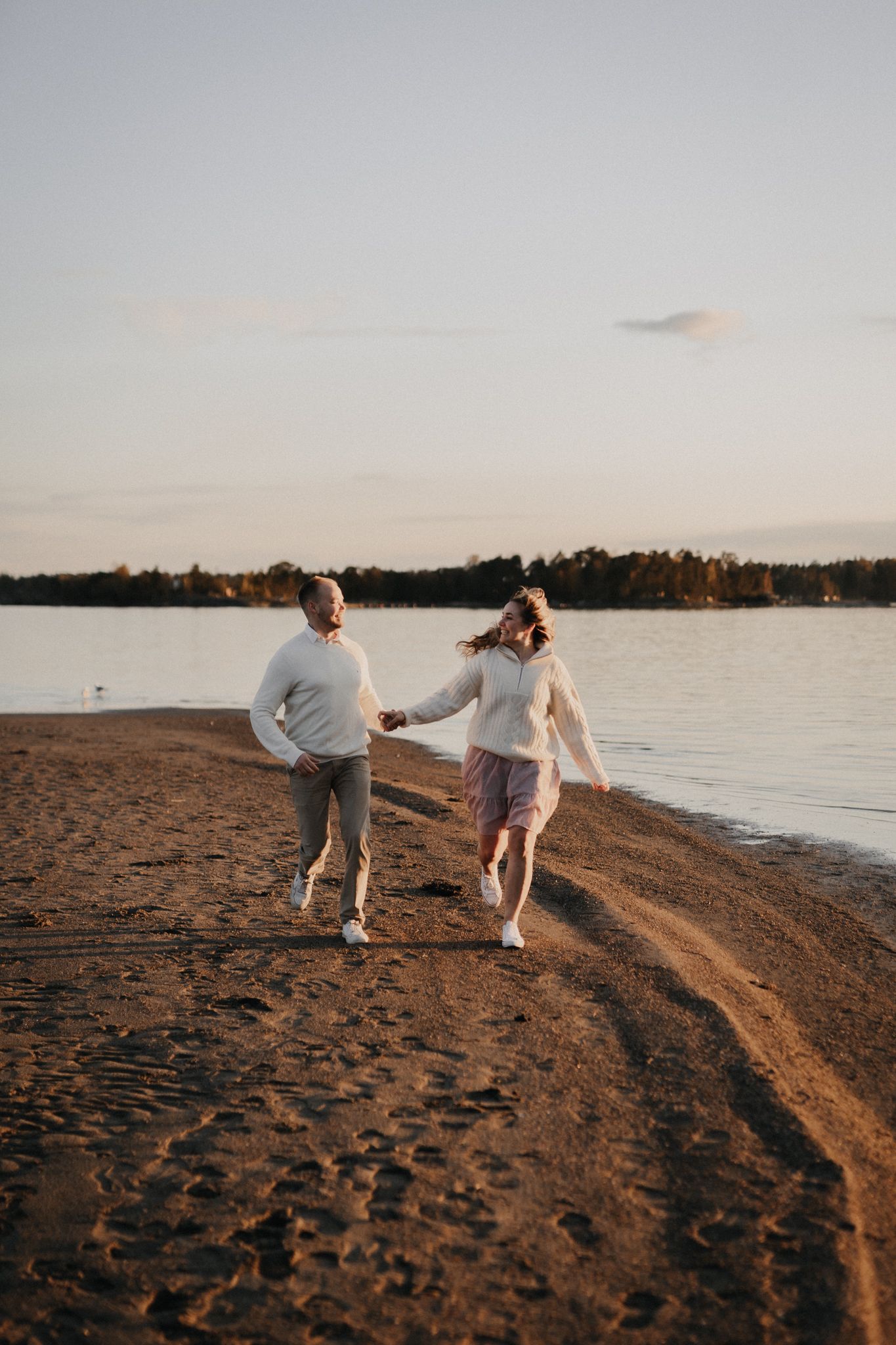 Happy couple runs hand-in-hand along a sandy beach shoreline during a warm golden sunset.
