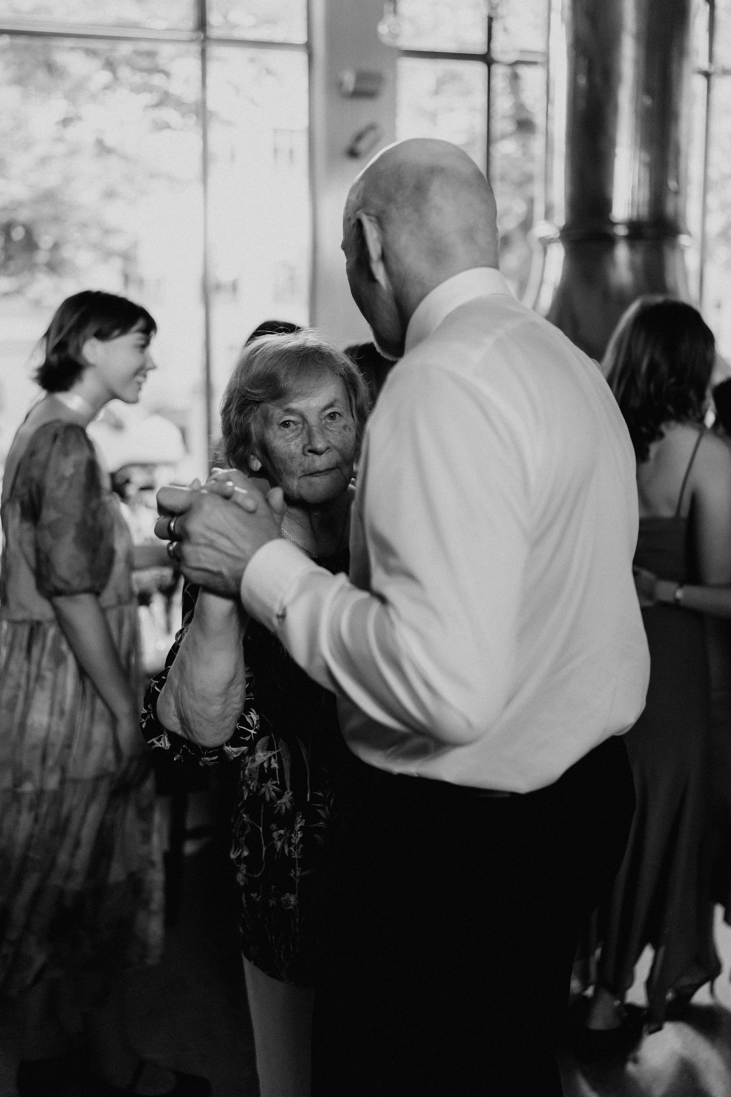 Elderly woman dances with bald man at a wedding reception in black and white.