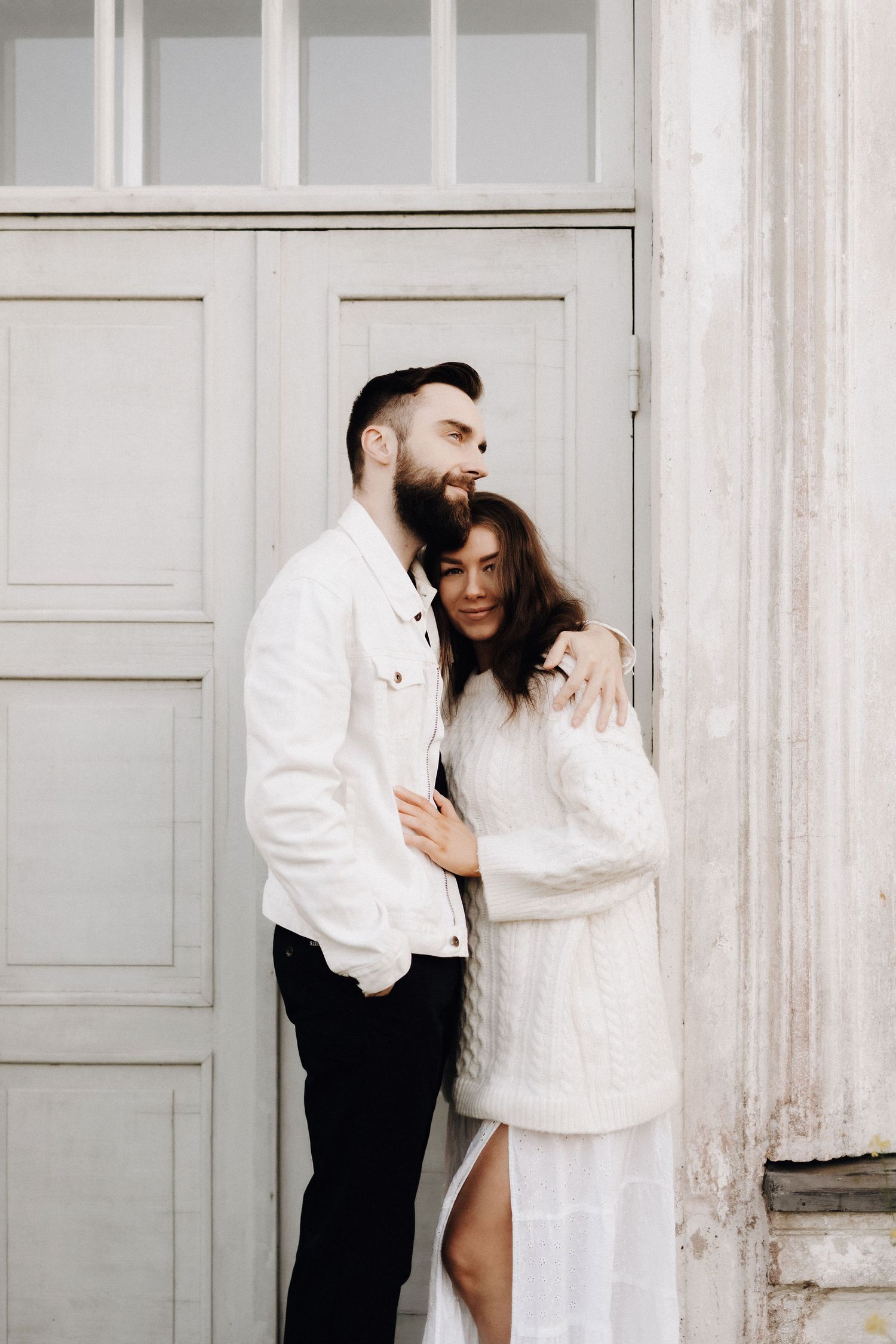Couple embracing and smiling together against elegant white vintage doors in soft light.