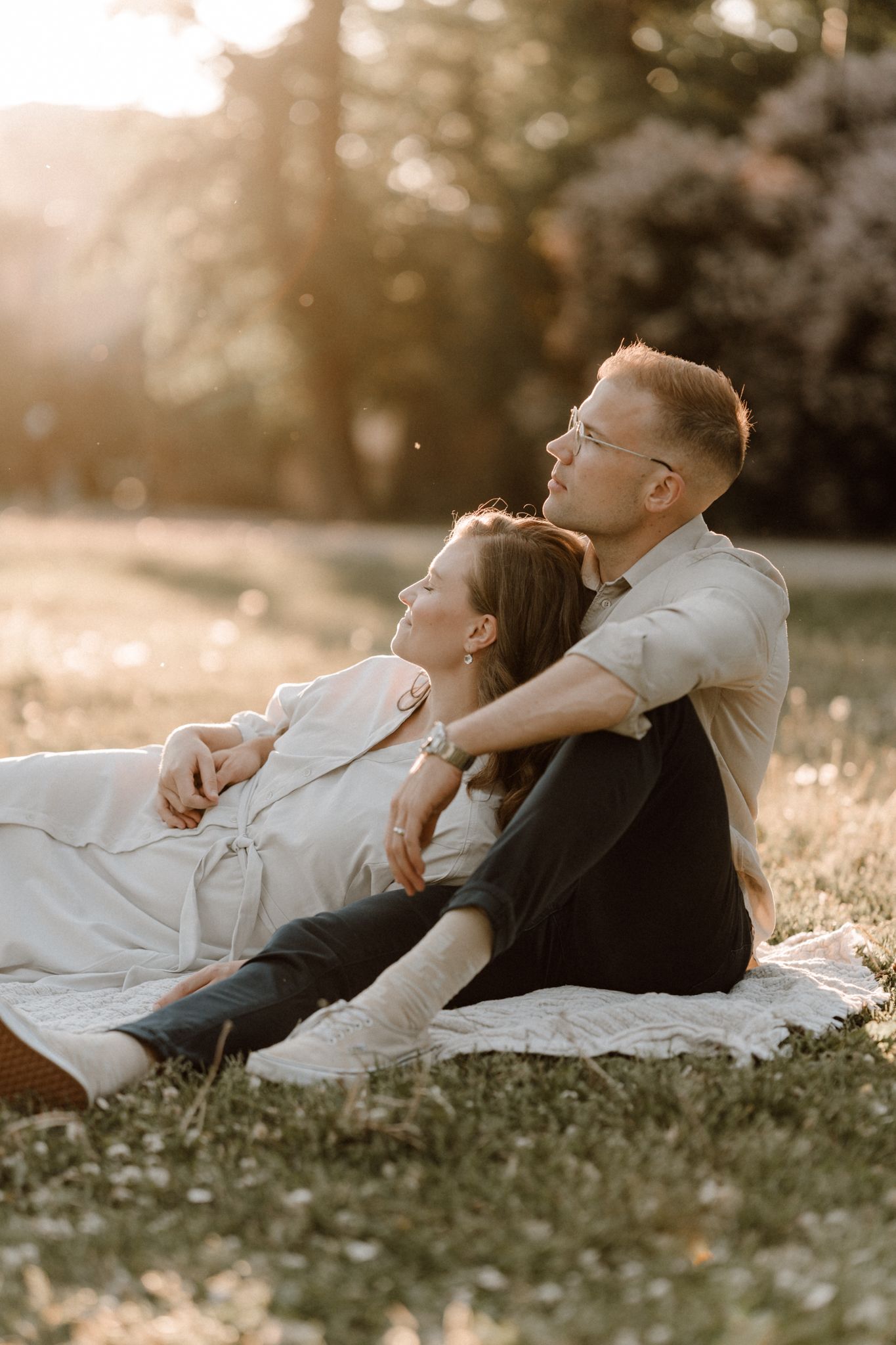 Couple relaxing on grass at golden hour sunset in a park, woman leaning on mans shoulder.