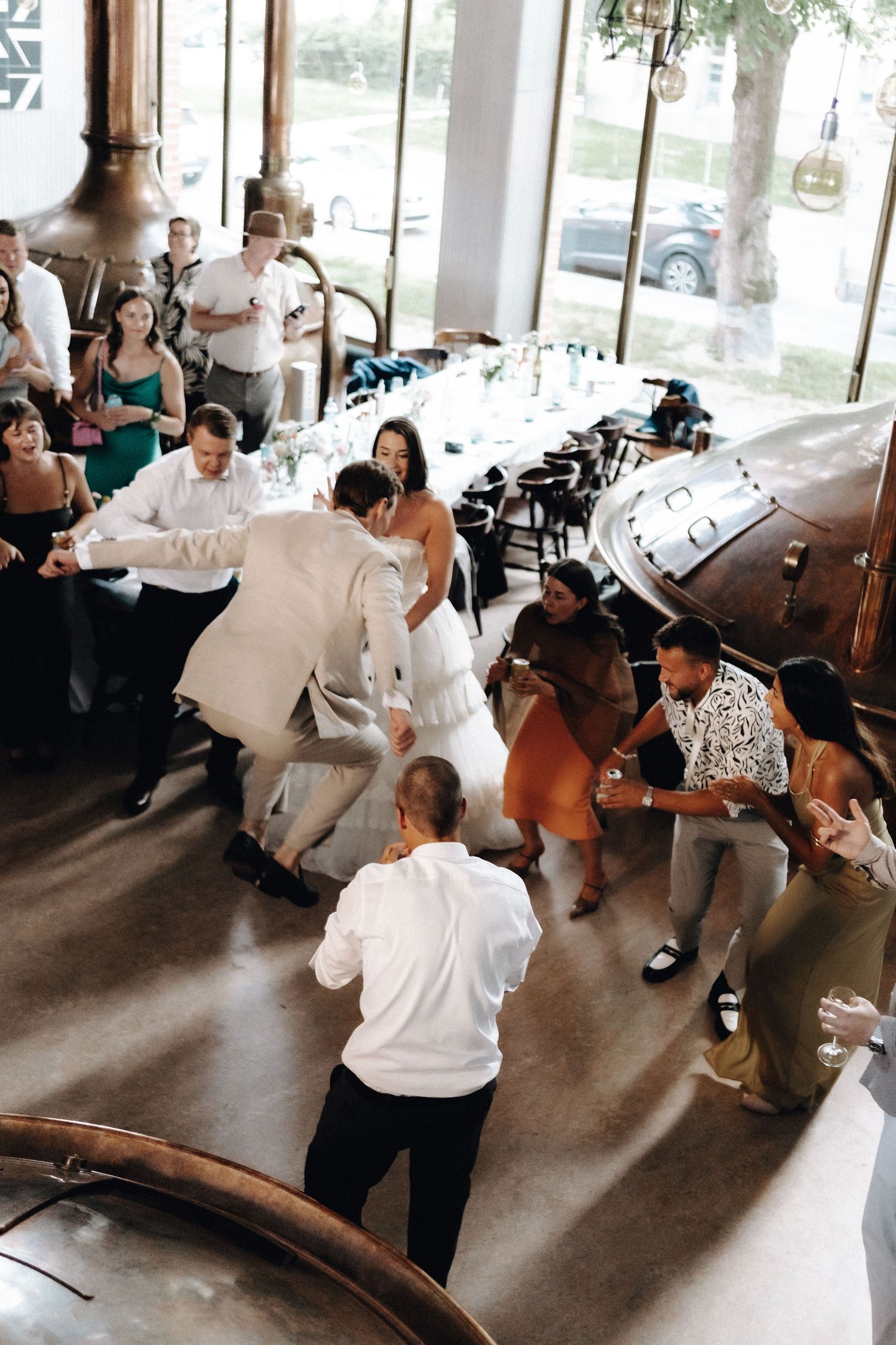 Aerial view of bride and groom dancing energetically with guests at brewery wedding.