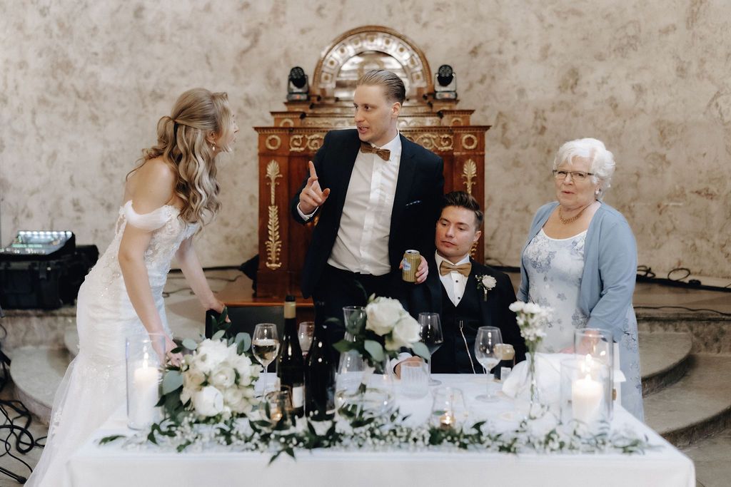 Groom gives a speech at the elegantly decorated wedding head table with floral arrangements.