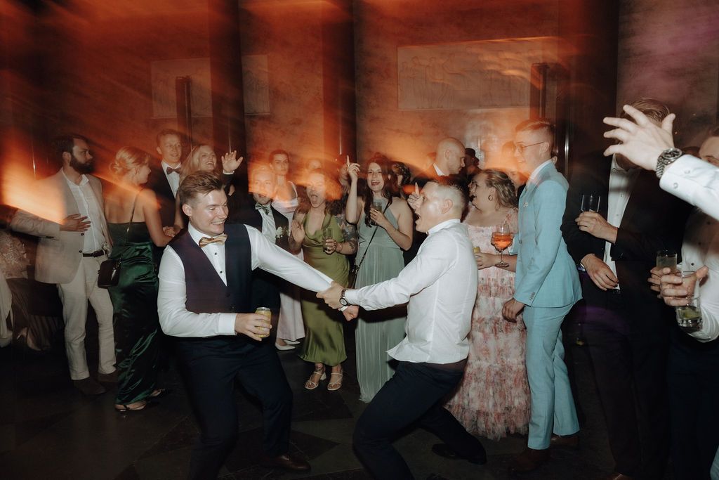Energetic wedding reception dance floor with guests celebrating and dancing together in a warmly lit venue.